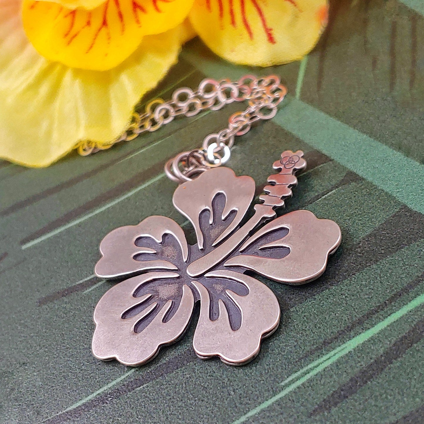 Sterling silver hibiscus necklace on a green background. Handmade by Smashfire Designs.