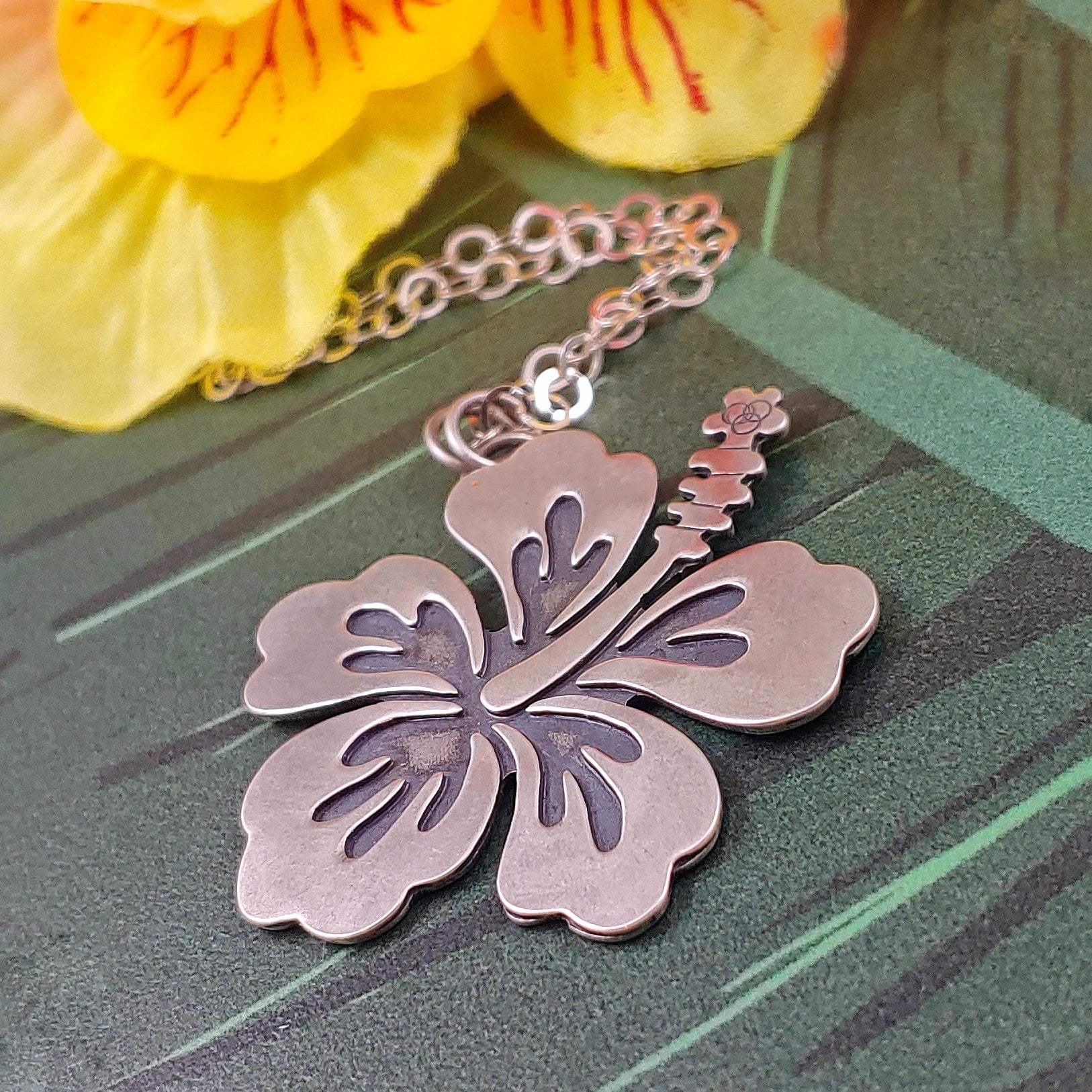 Sterling silver hibiscus necklace on a green background. Handmade by Smashfire Designs.