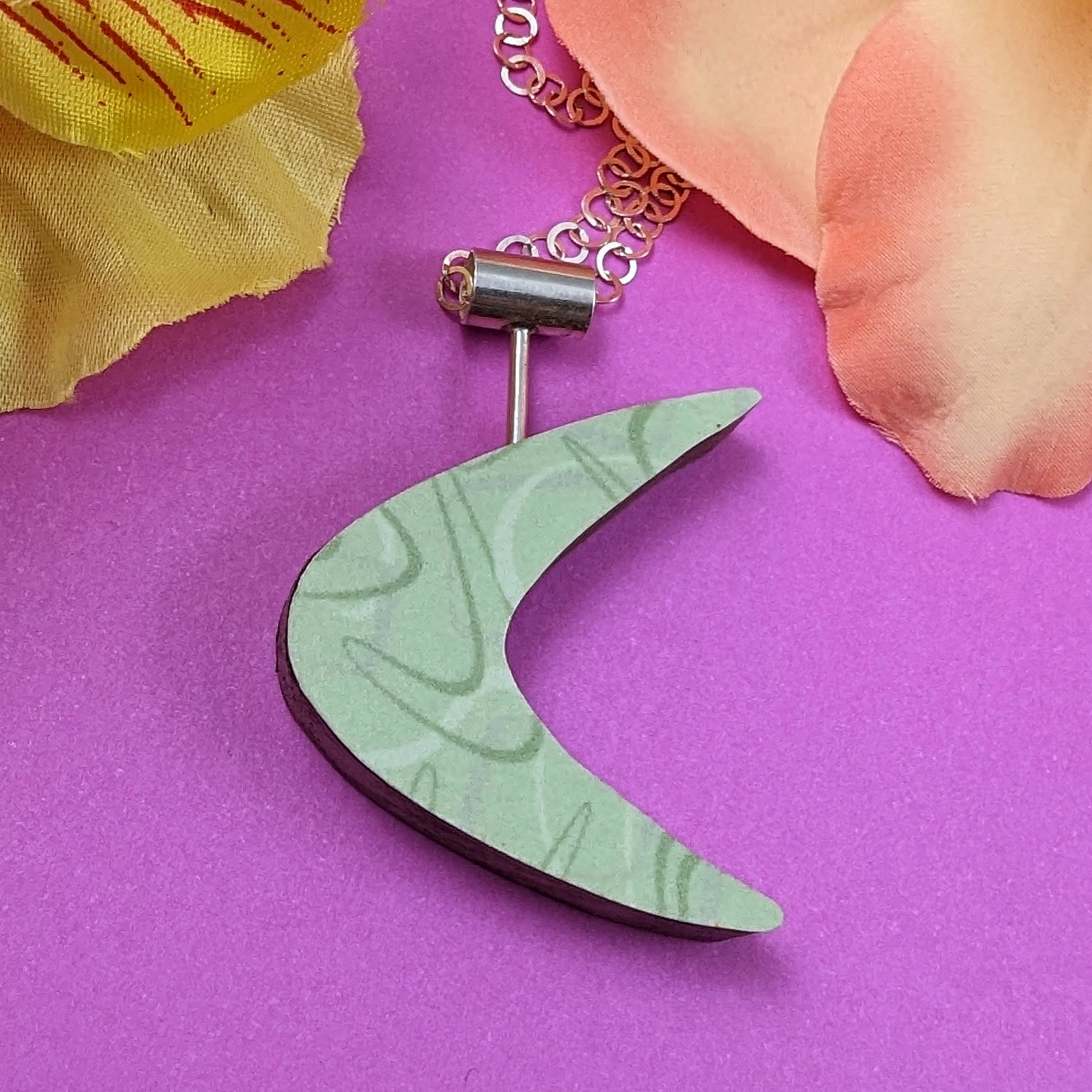 Boomerang shaped laminate on wood necklace on a pink background