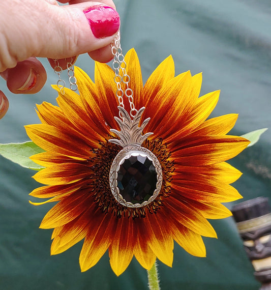 hand holding a rosecut black onyx pineapple in front of sunflower