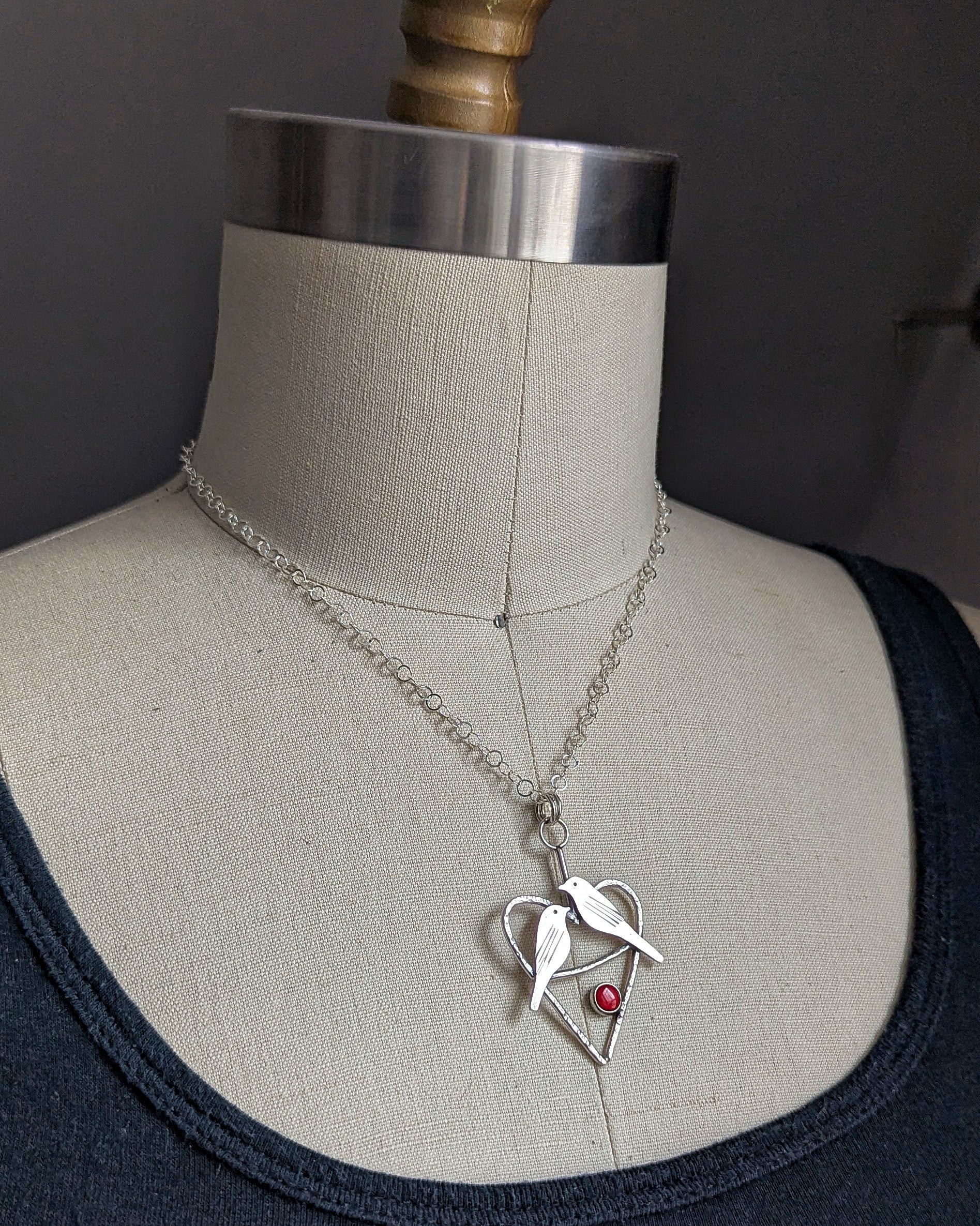 Mid century modern birds handmade in sterling silver in a heart with a coral red stone necklace shown on a dress form