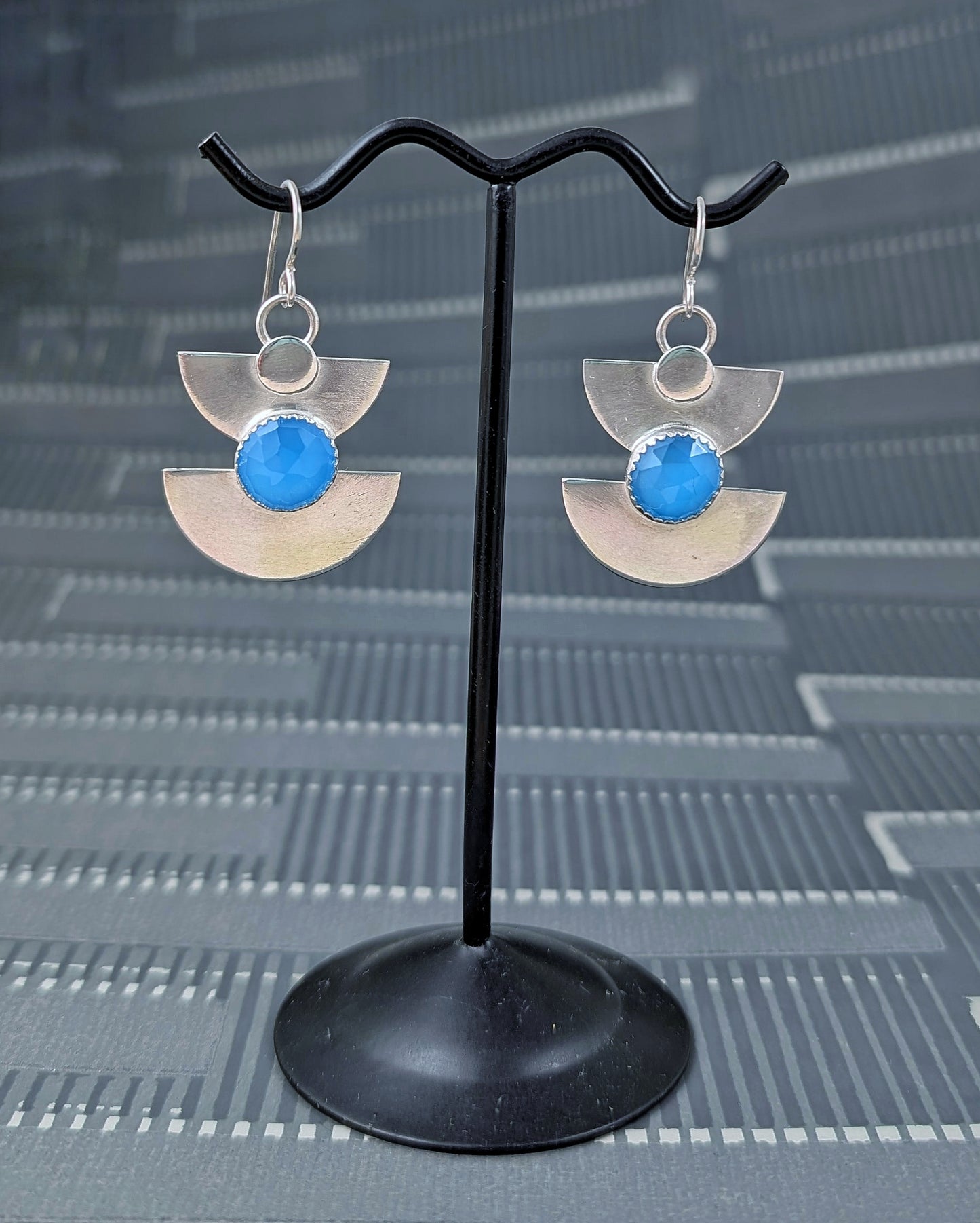 Close up of sterling silver half moon earrings with blue chalcedony on an earring stand