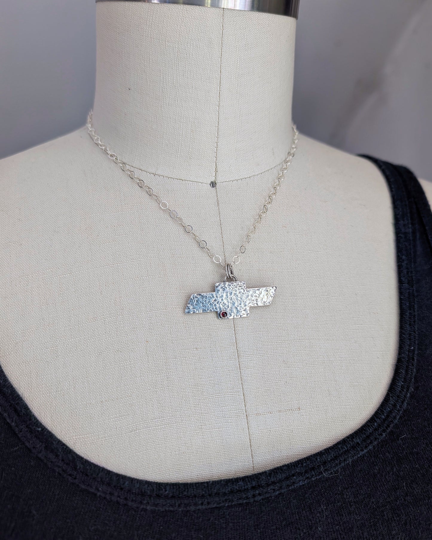 Sterling silver Chevrolet bowtie necklace on a mannequin facing sideways.