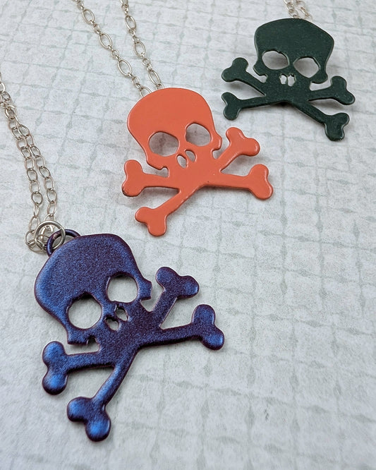 Three colorful skull and crossbones pendants on a textured surface