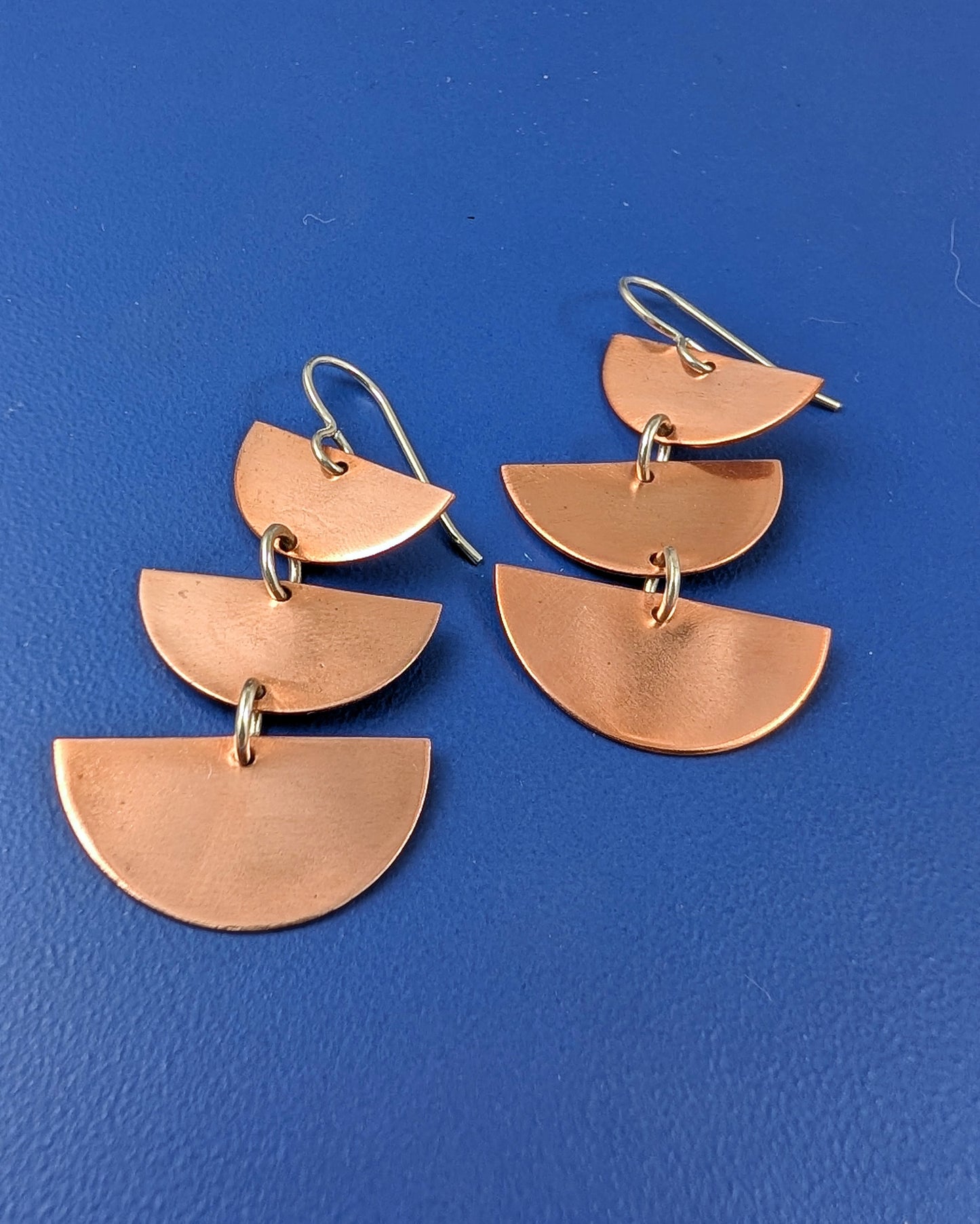 Copper half moon dangle earrings on a blue background