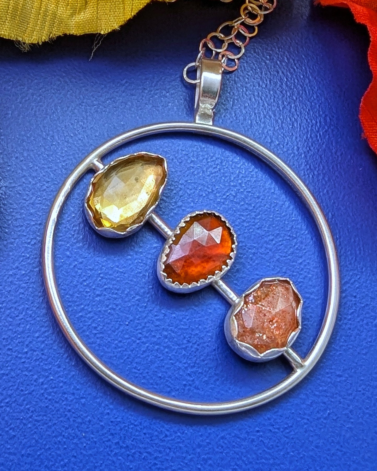 Rosecut citrine, garnet, sunstone on a sterling silver circle shown on a blue background