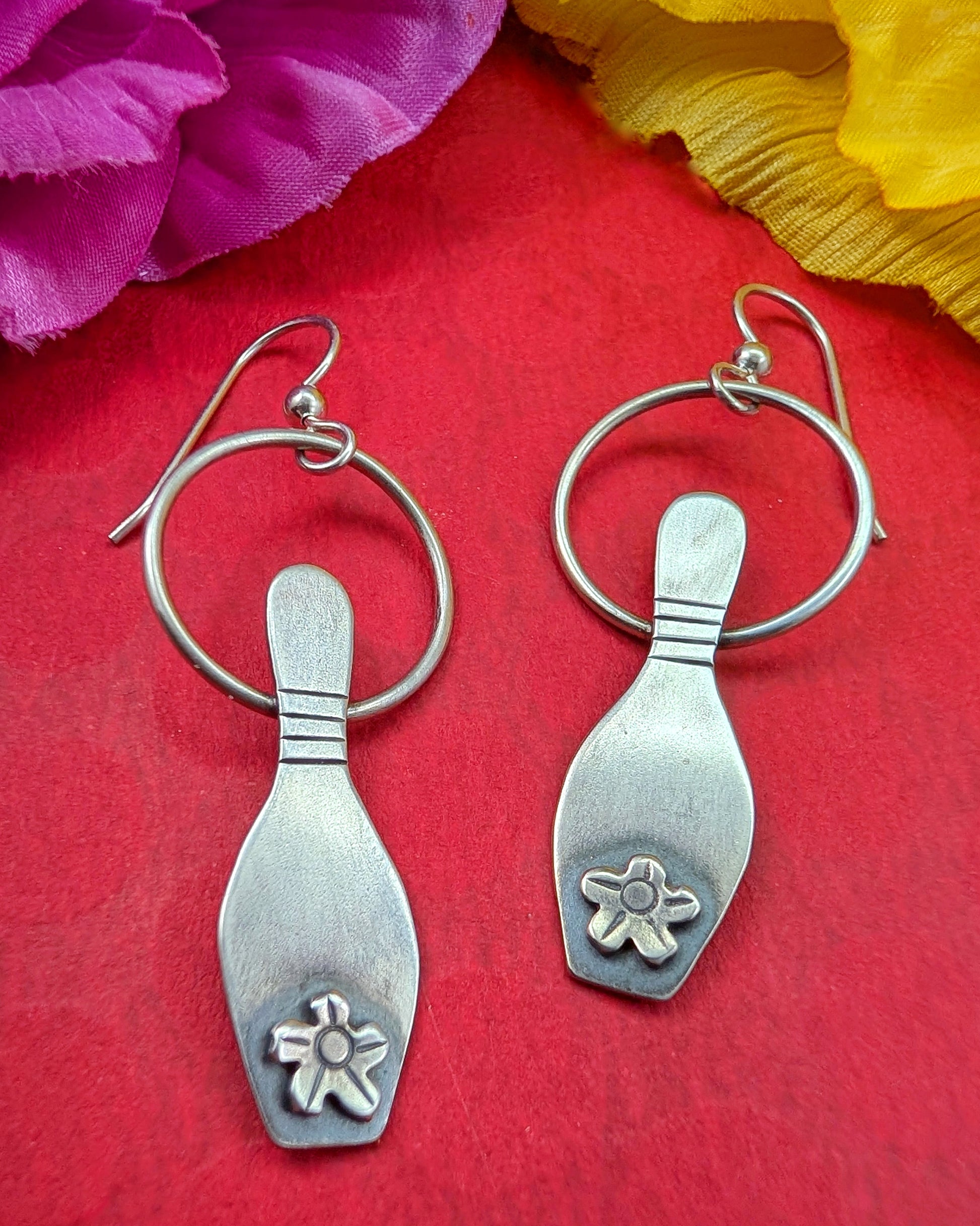 Sterling silver bowling pin earrings on a red background