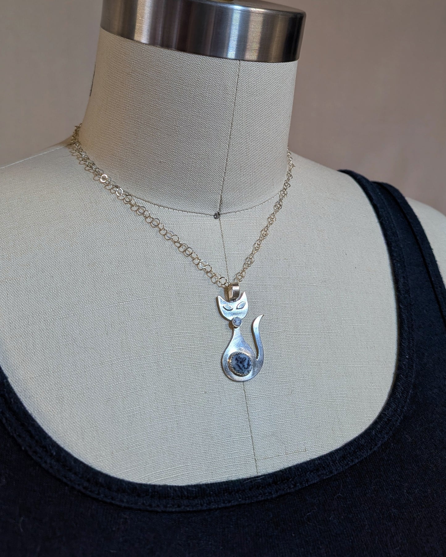 Handmade sterling silver retro cat necklace with black and white dendritic opal stone on a dress form.
