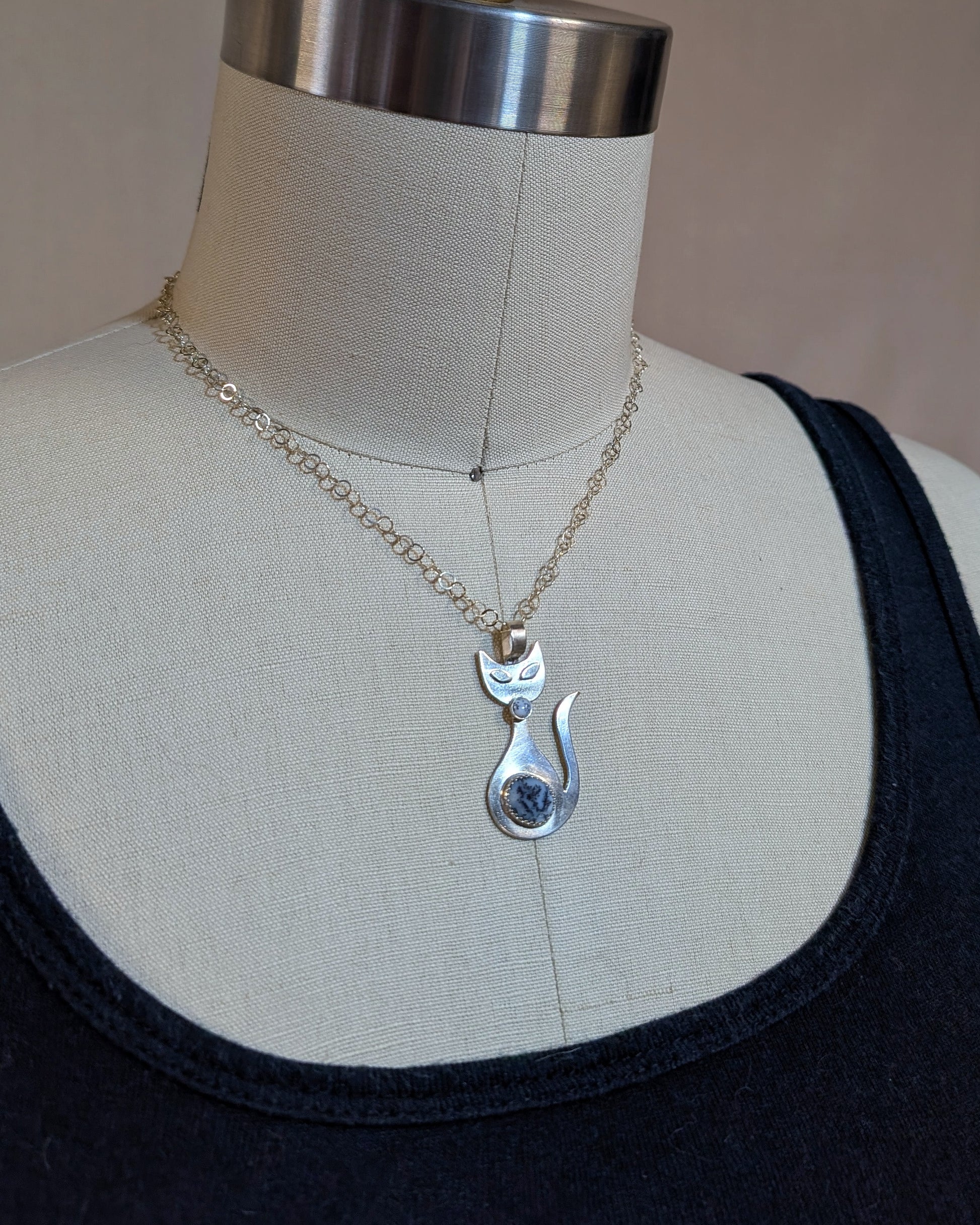 Handmade sterling silver retro cat necklace with black and white dendritic opal stone on a dress form.