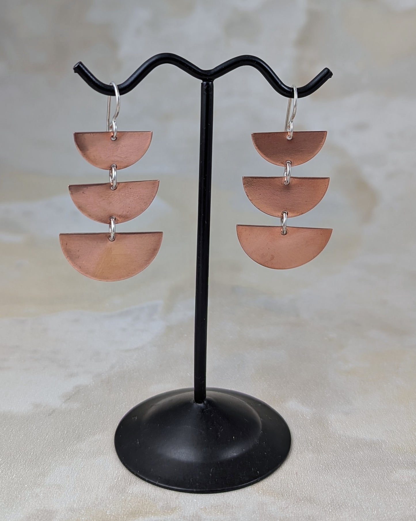 Copper half moon dangle earrings on an earring stand