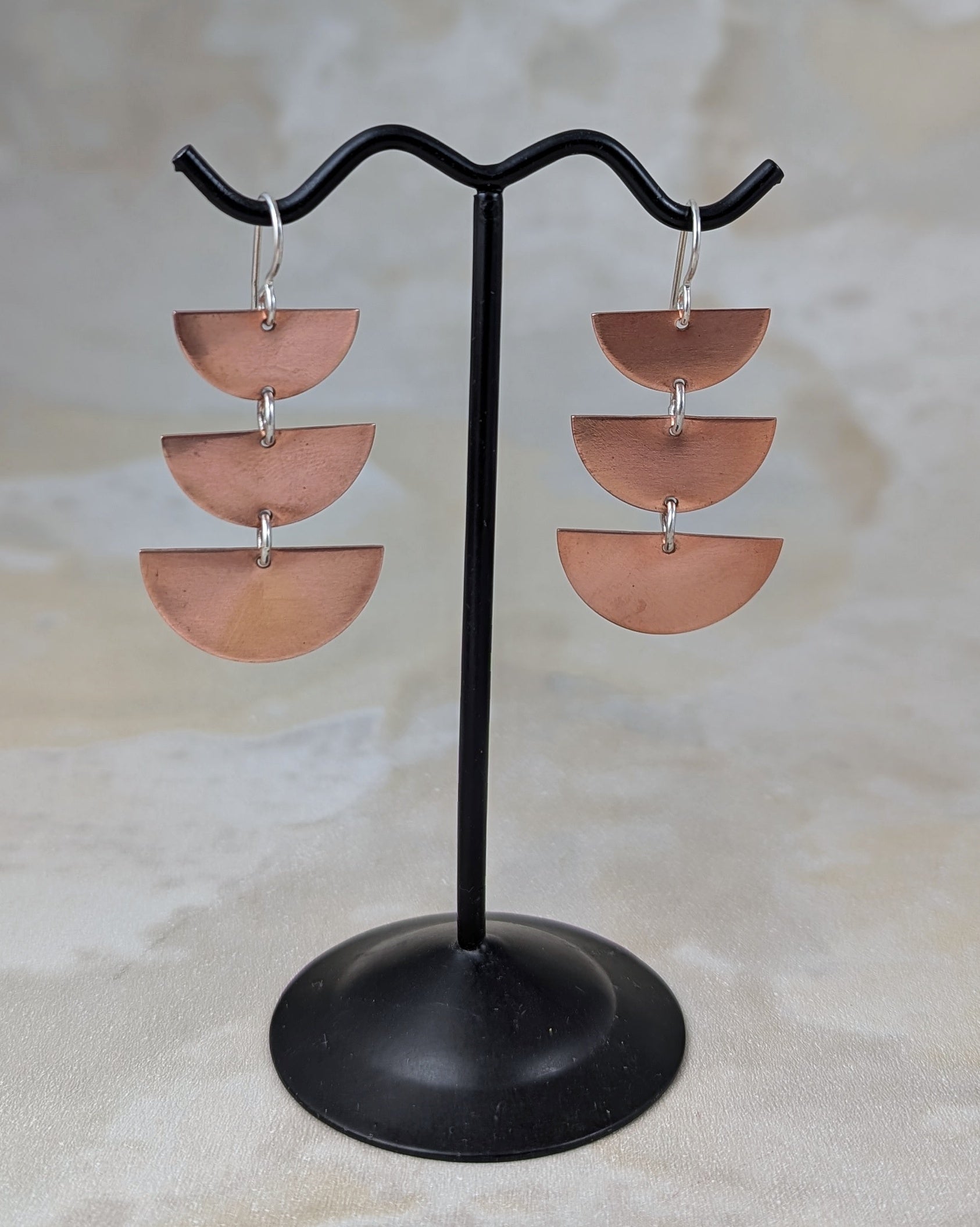Copper half moon dangle earrings on an earring stand