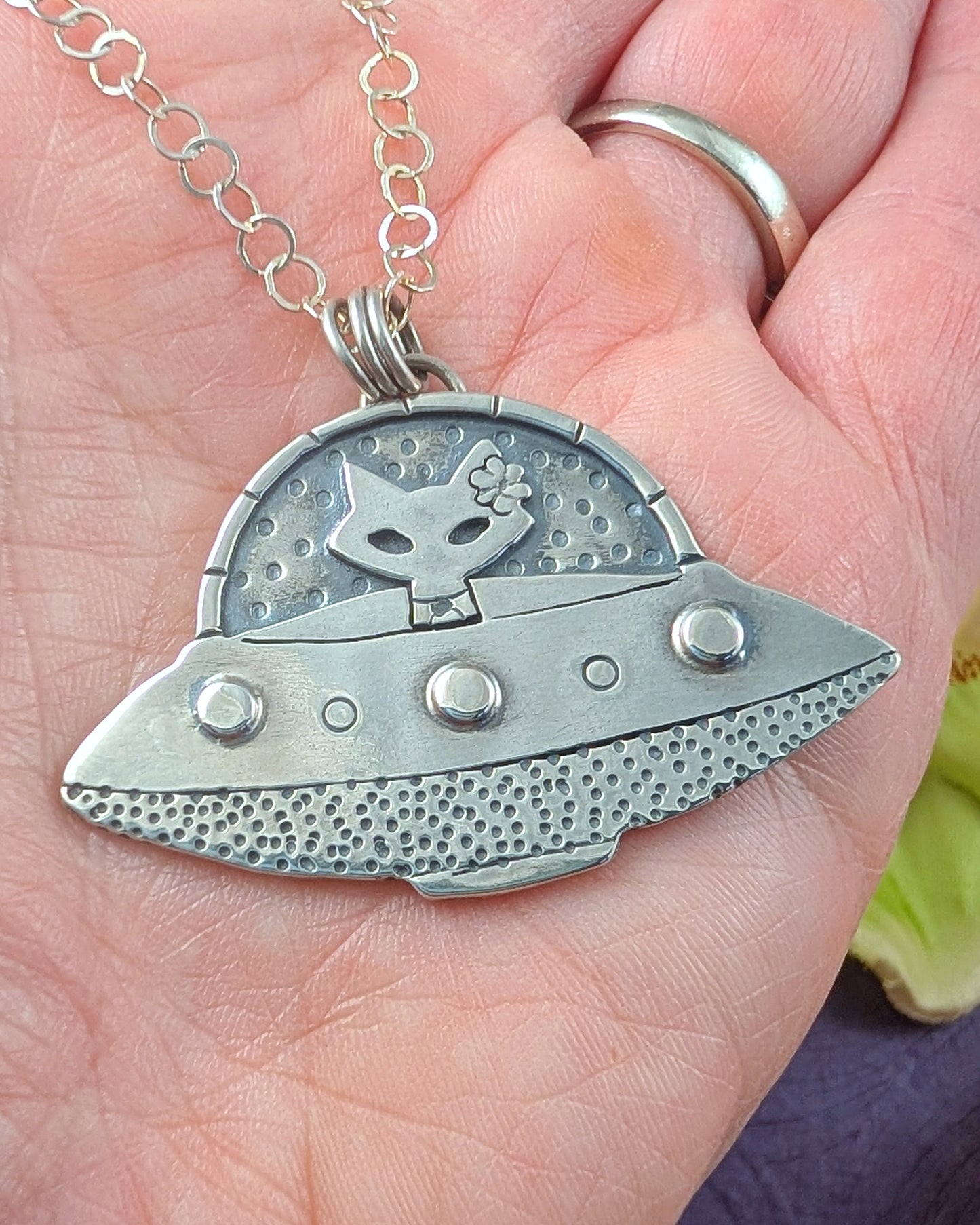 Sterling silver UFO necklace with a mid century modern cat at the helm shown in a human's hand