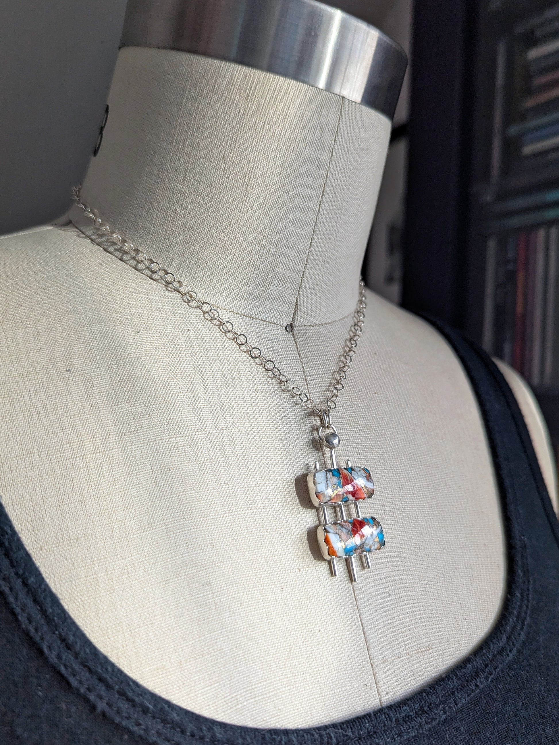 Mid century modern necklace with turquoise mosaid and sterling silver on a dress form at a side angle