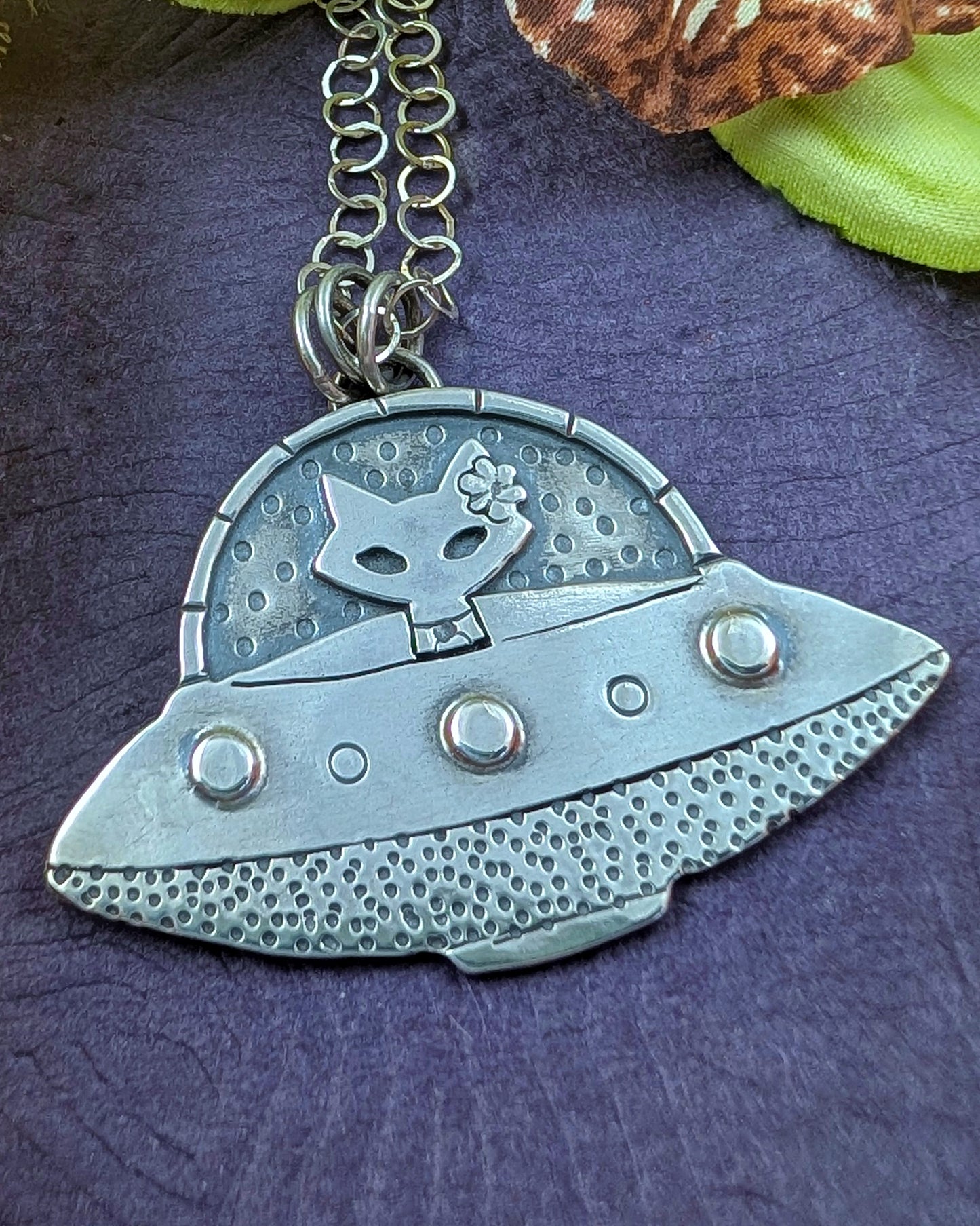Mid century modern sterling silver UFO  spaceship necklace with a mid century modern cat in the driver seat on a purple background