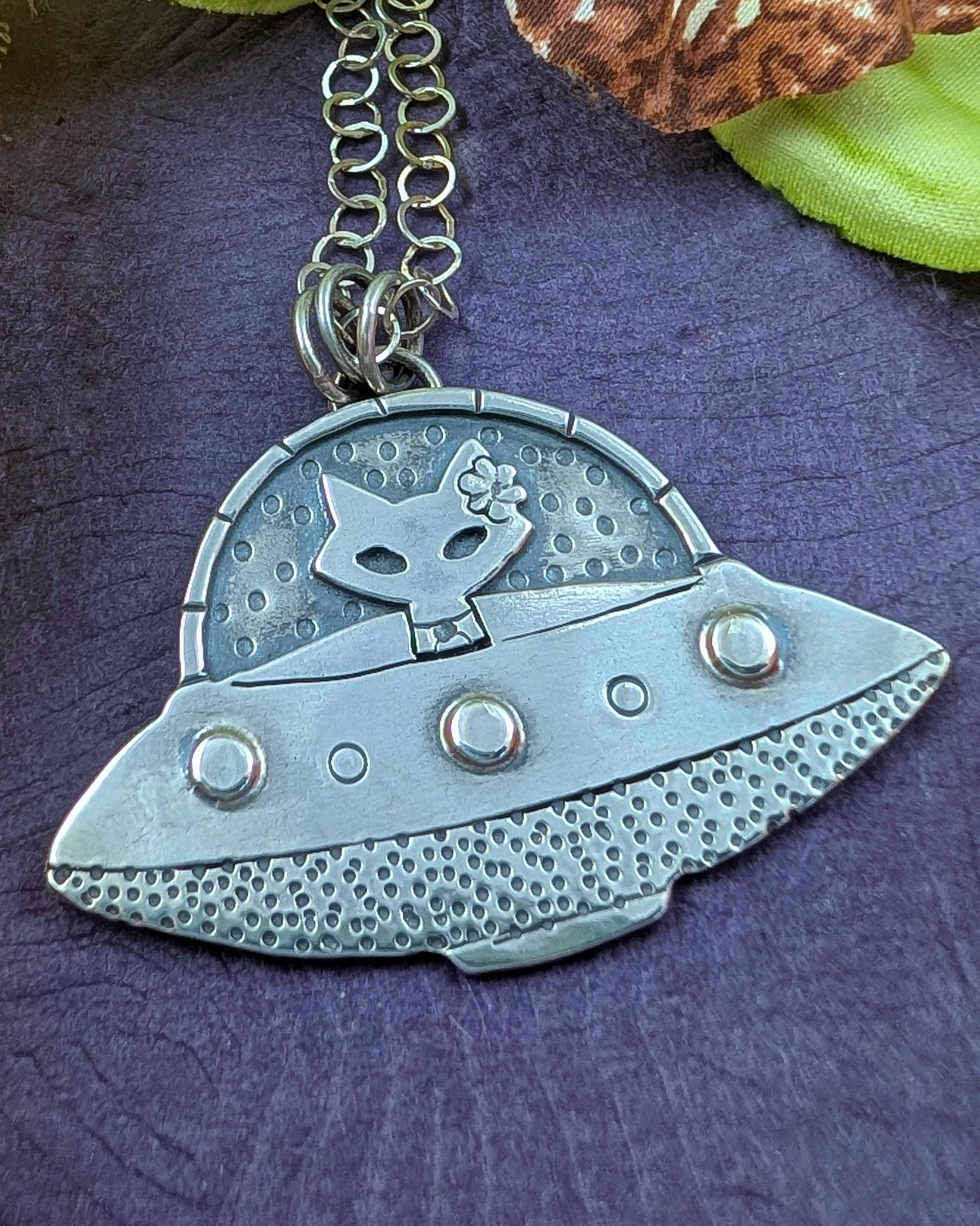 Mid century modern sterling silver UFO  spaceship necklace with a mid century modern cat in the driver seat on a purple background