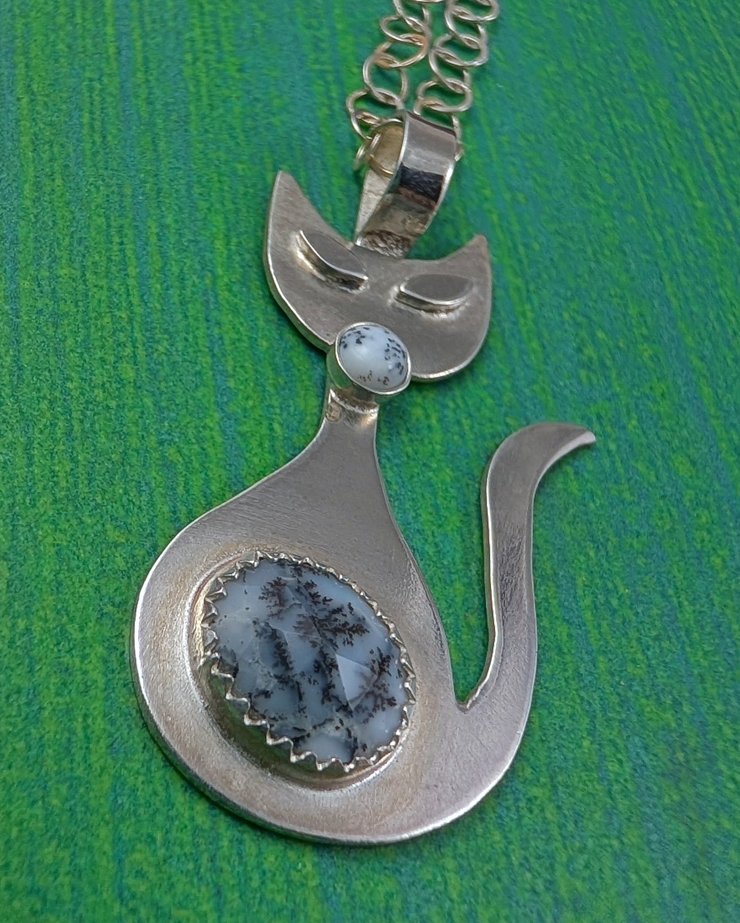 Handmade sterling silver retro cat necklace with black and white dendritic opal stone on a green background