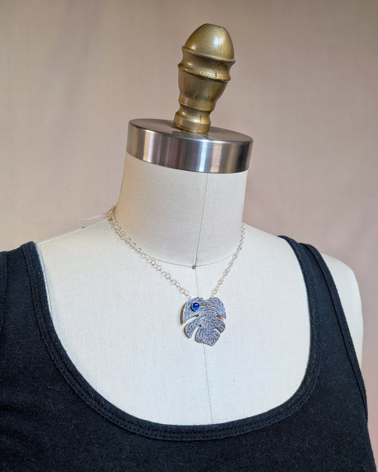 Sterling silver monstera leaf necklace with blue cat's eye on a dress form