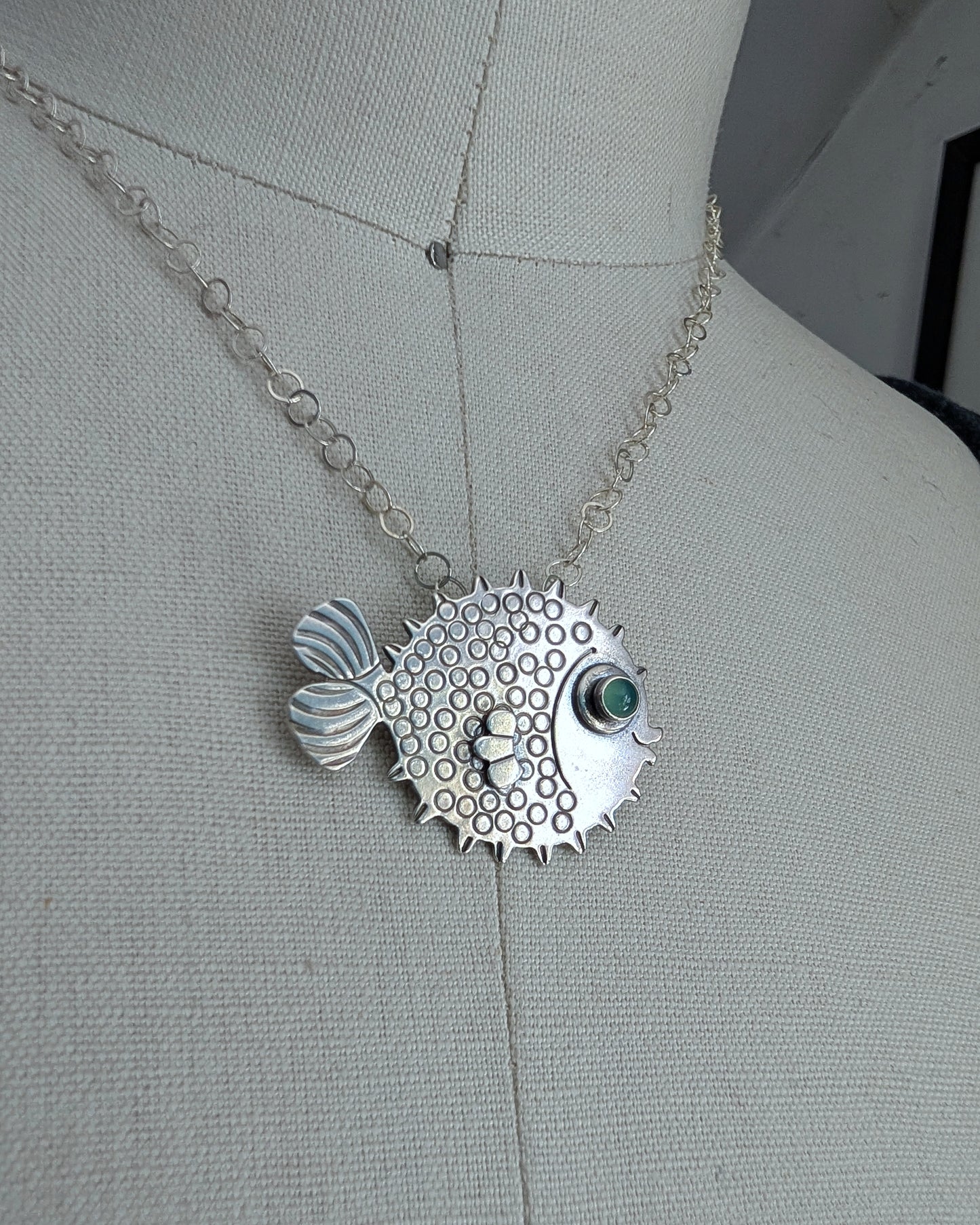 Blowfish necklace in sterling silver with a green chrysoprase eye on a dress form. Close up image.