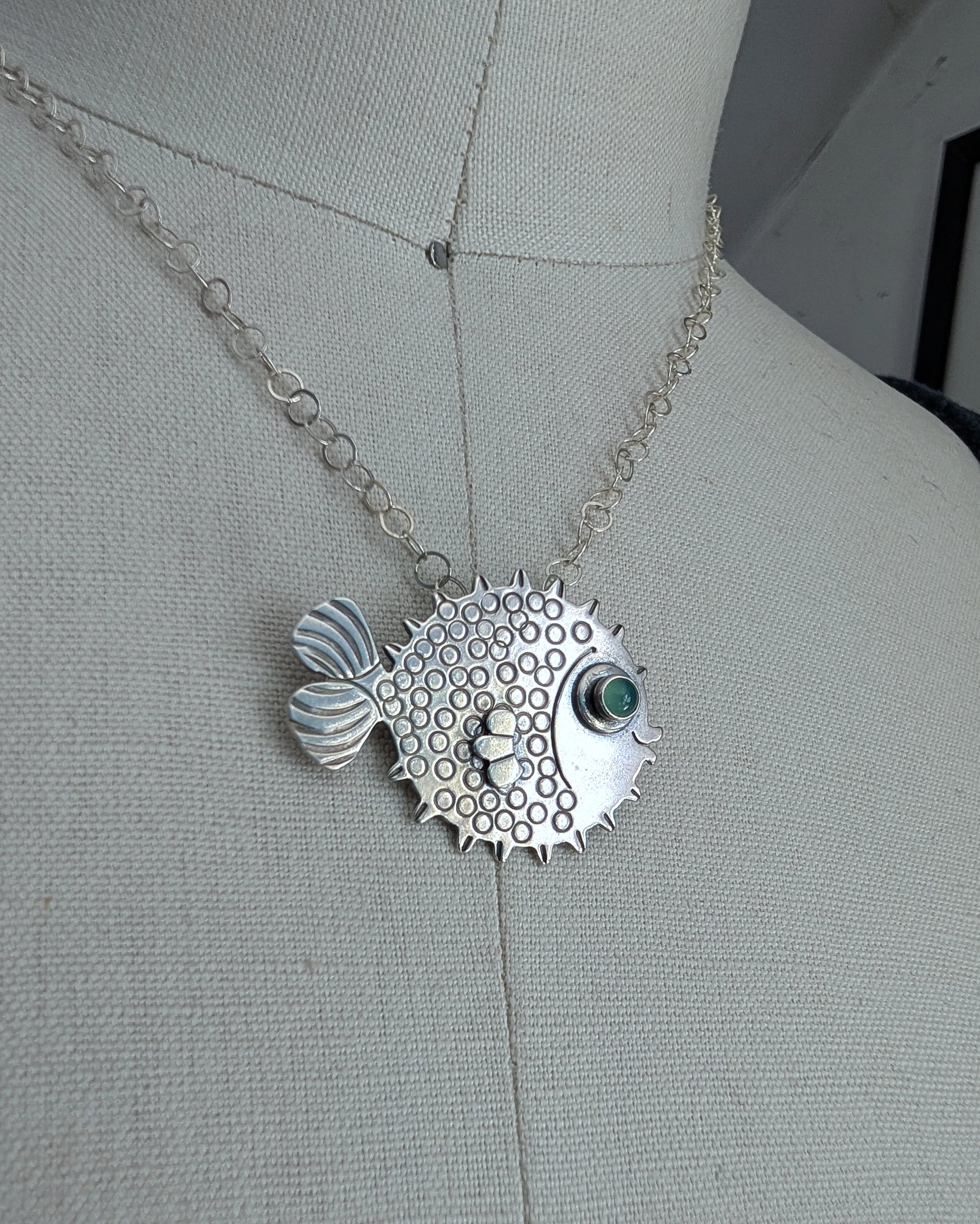 Blowfish necklace in sterling silver with a green chrysoprase eye on a dress form. Close up image.