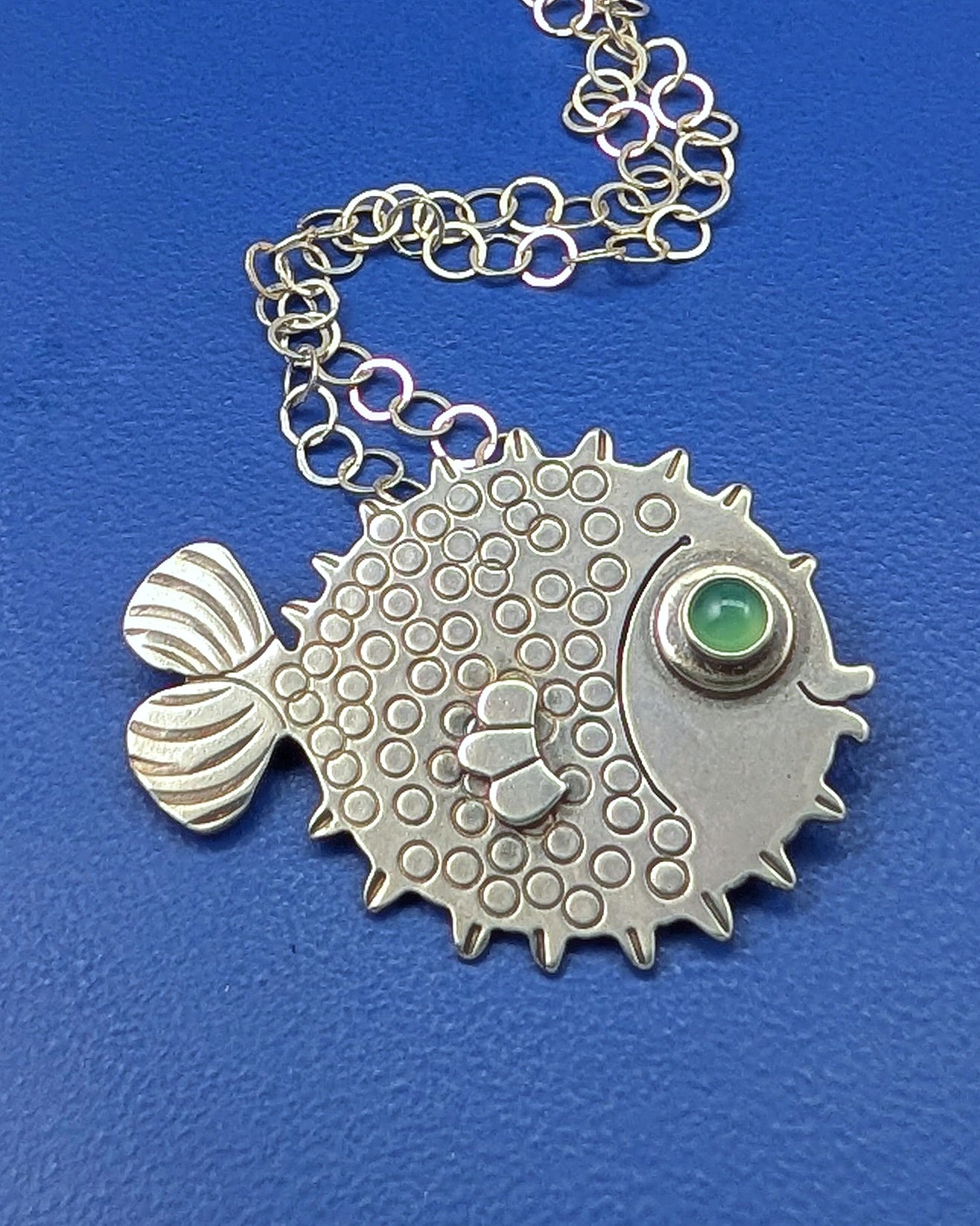 Sterling silver puffer fish necklace with chrysoprase eye on blue background