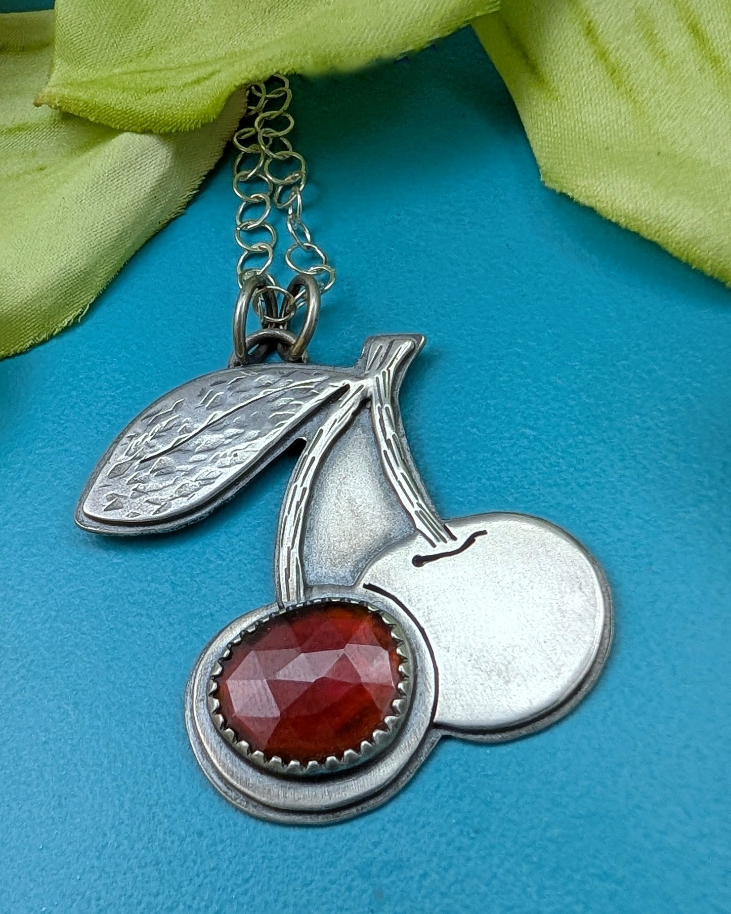 Sterling silver cherries necklace with rosecut red garnet on a turquoise background