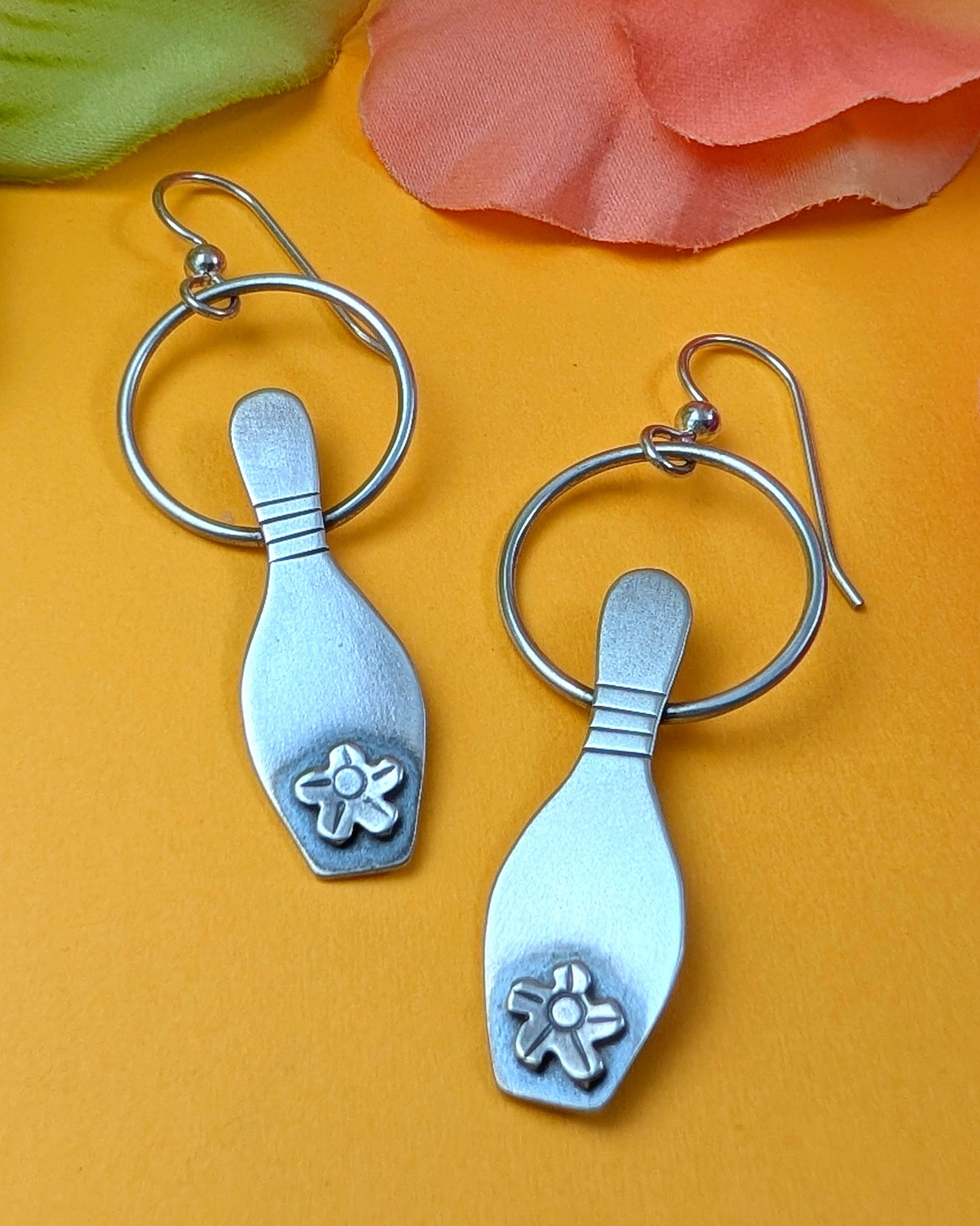 Sterling silver bowling pin earrings on a yellow background.