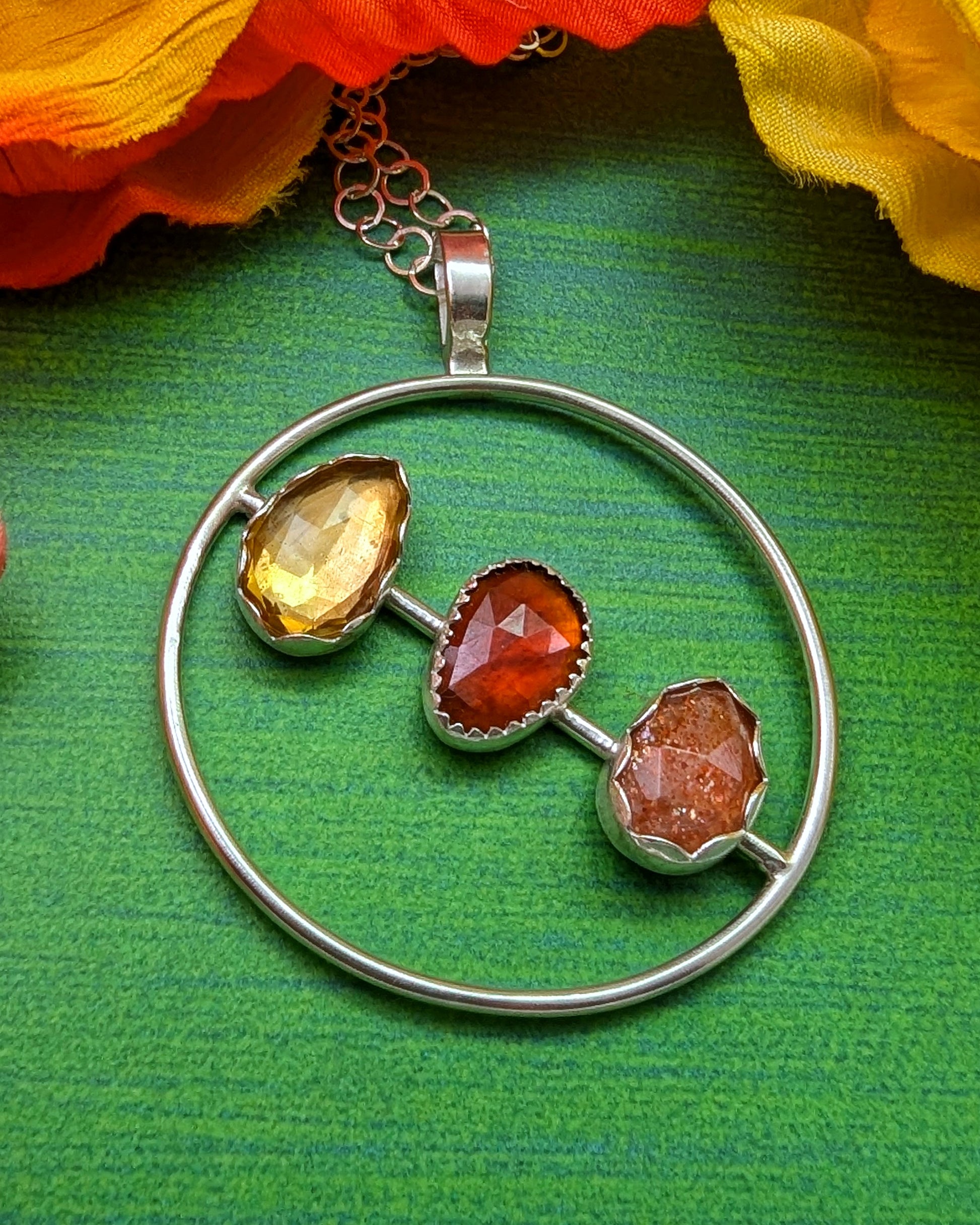 Sterling silver circle necklace with rosecut citrine, garnet, and sunstone shown on a green background