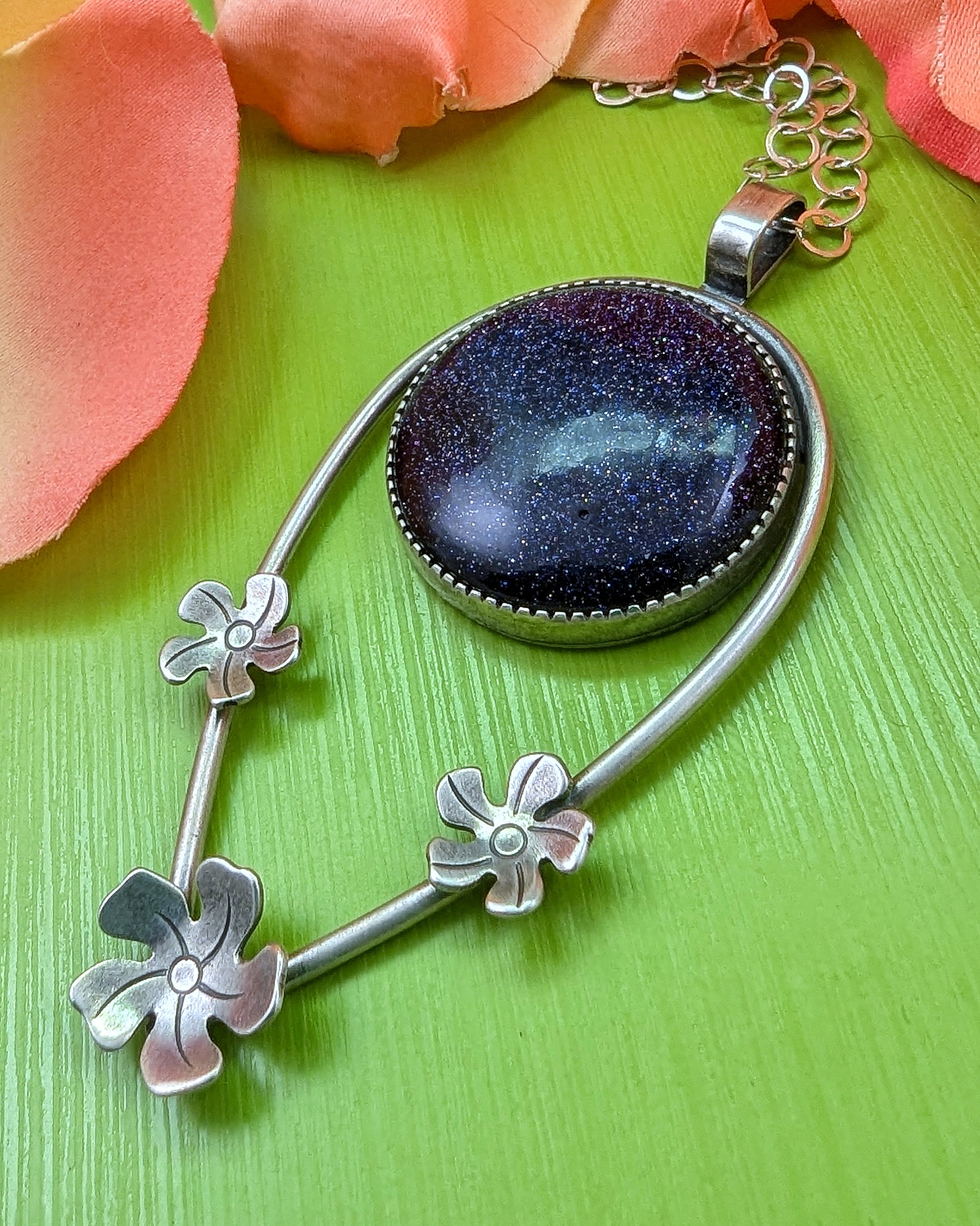 Side view of sterling silver Tiki necklace featuring plumeria flowers and blue goldstone