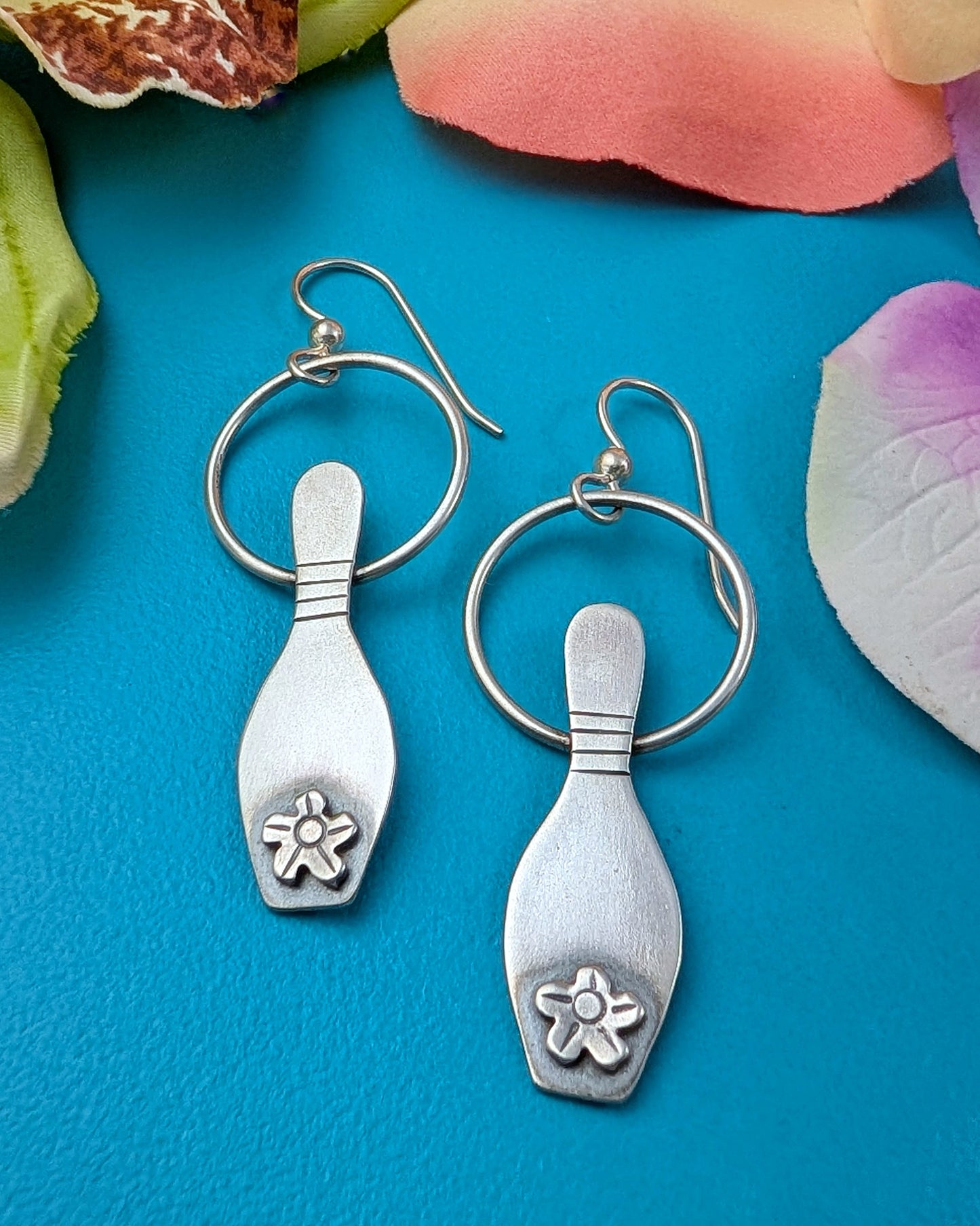 Sterling silver bowling pin earrings on a blue background with floral elements.