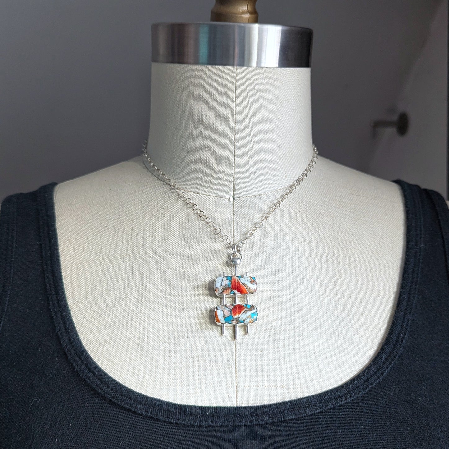 Handmade mid century modern necklace in sterling silver with turquoise mosaic stones shown on a dress form 