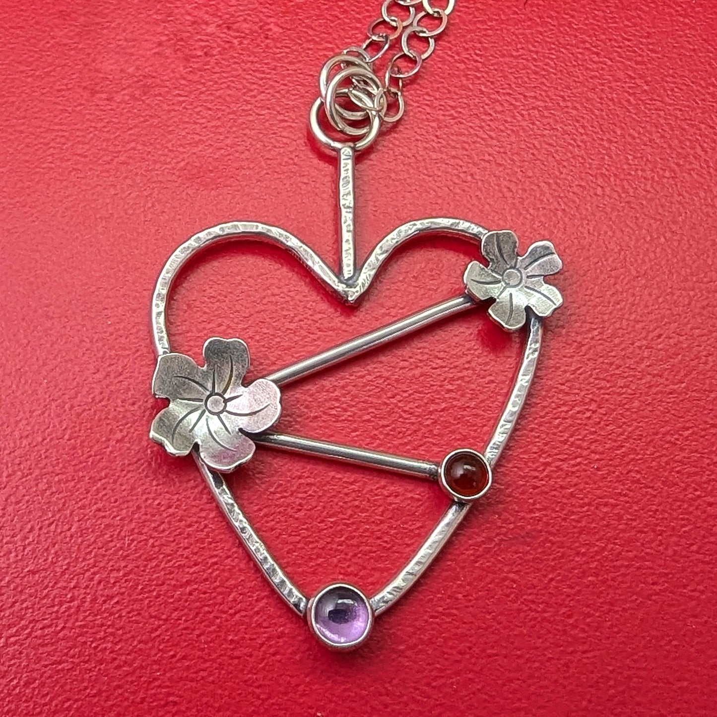 Sterling silver handmade heart necklace with Tiki plumeria flower details and carnelian and pink stones on a red background