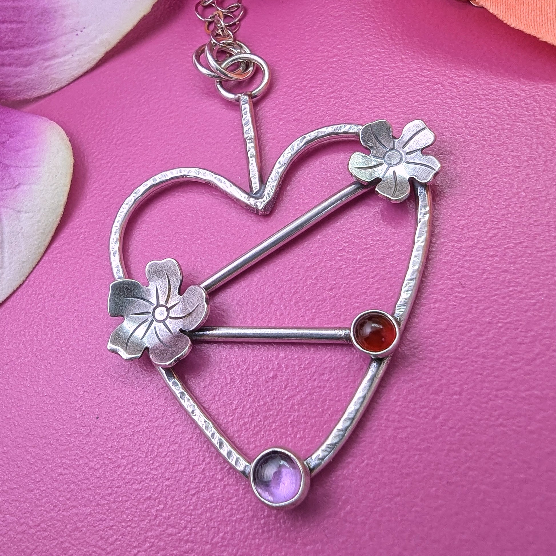 Sterling silver handmade heart necklace with Tiki plumeria flower details and carnelian and pink stones shown on a pink background