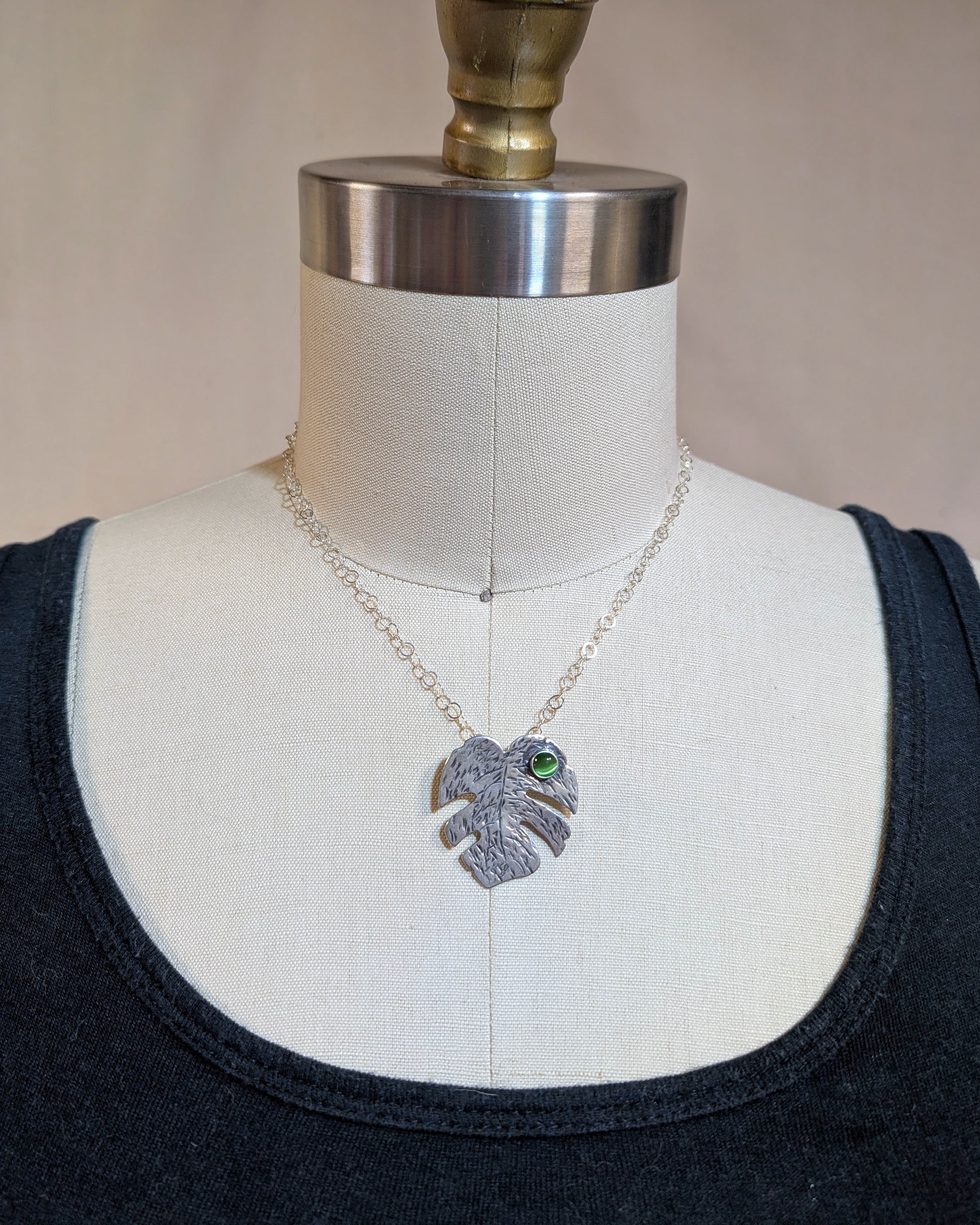 Sterling silver monstera leaf necklace with green cats eye on dress form.