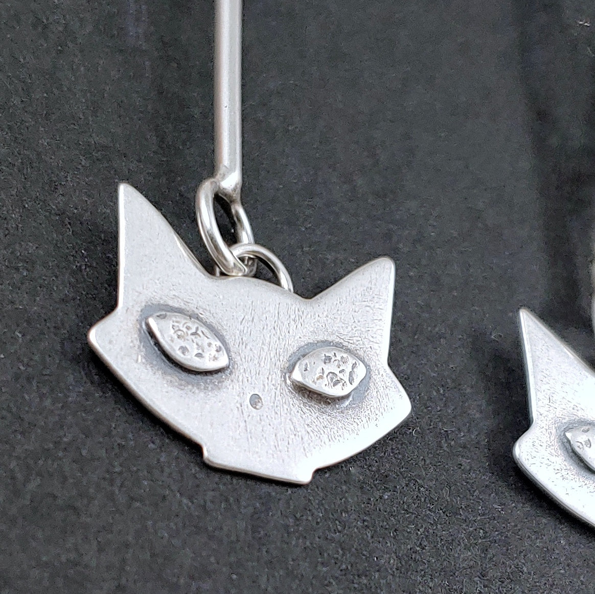 Close up of sterling silver mid mod cat head earring on black background.