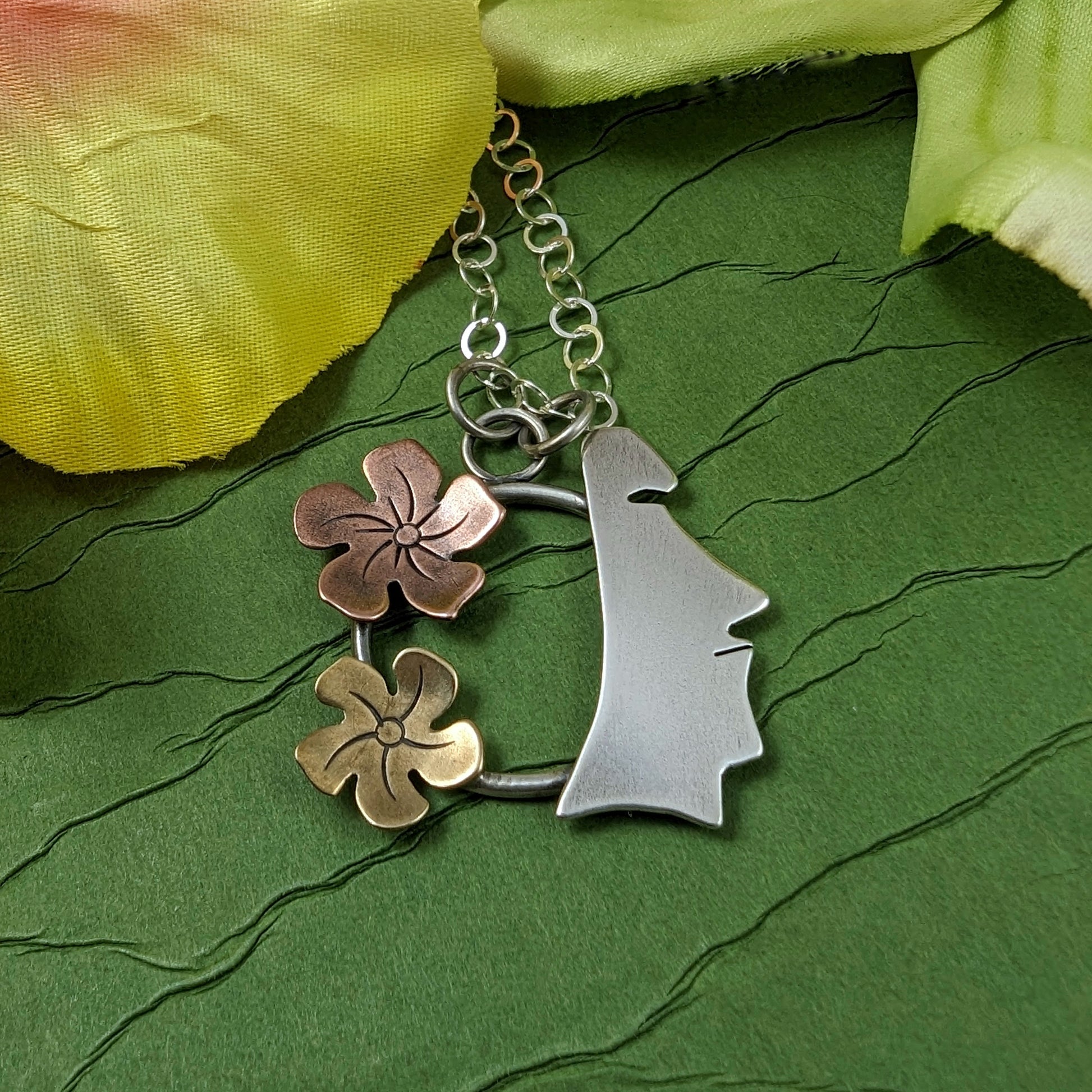 Sterling silver, copper, and brass necklace on a green background with flowers