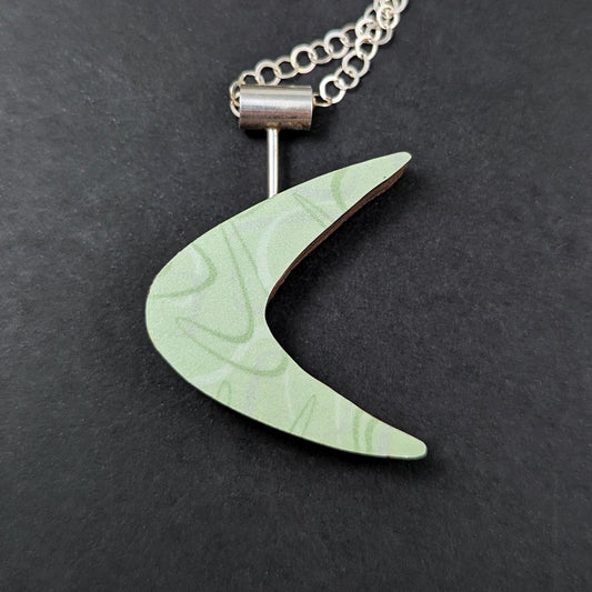 Boomerang shaped laminate on wood necklace on a black background