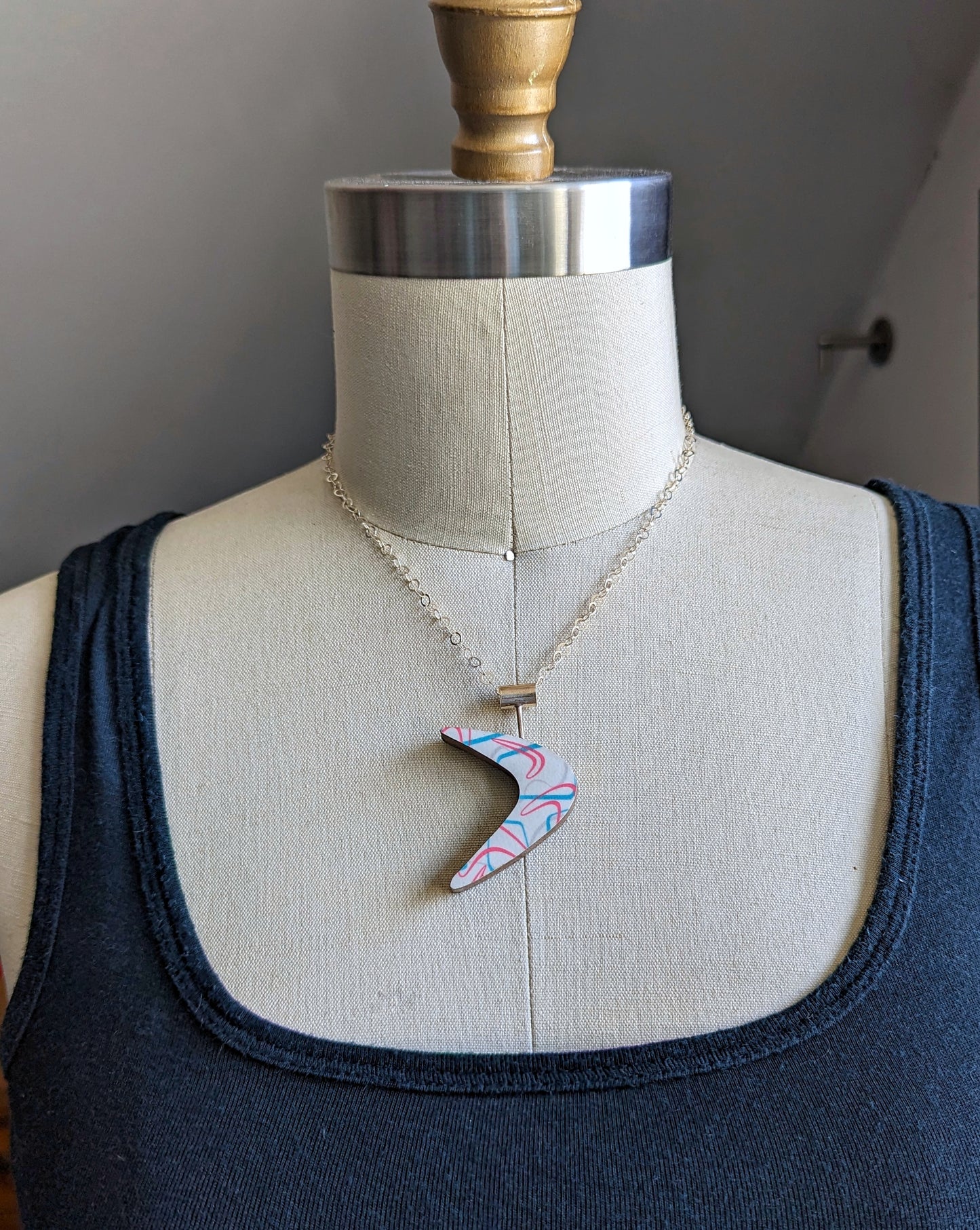 Boomerang shaped laminate on wood necklace on dress form to show how it looks on