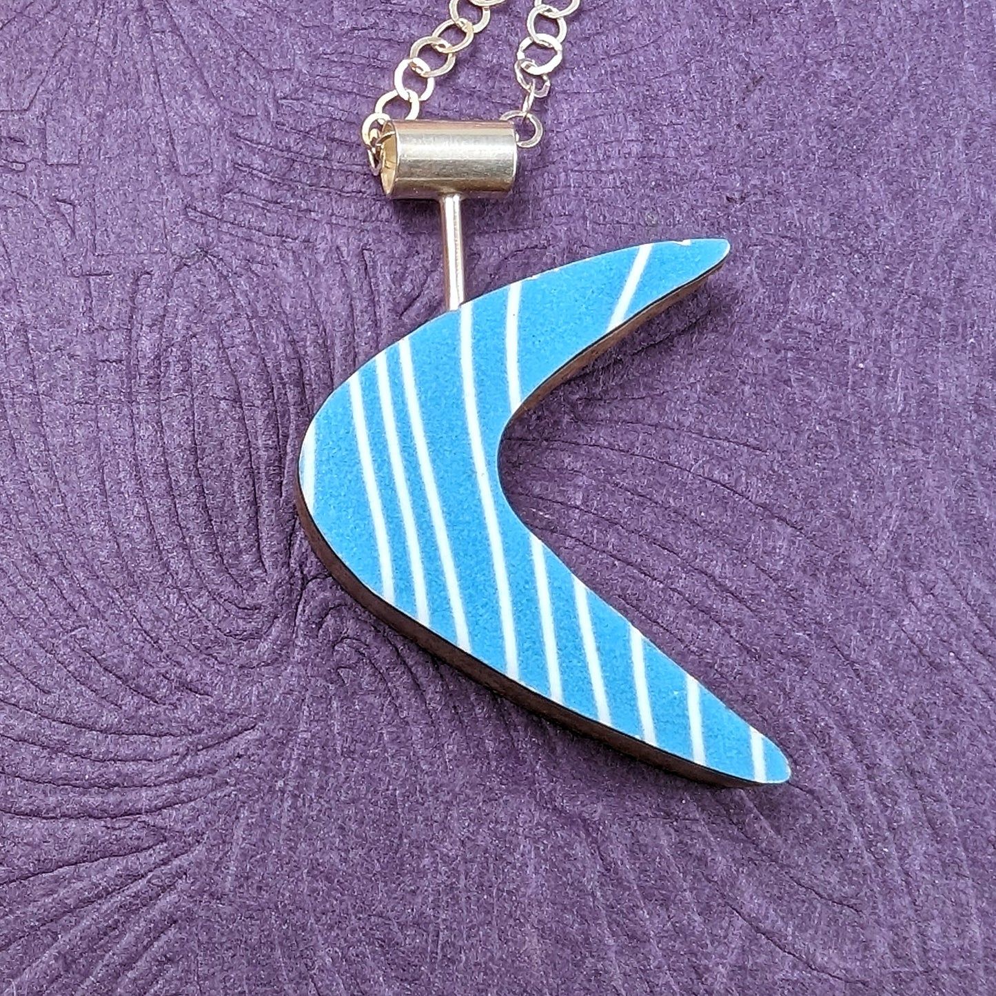 Boomerang shaped laminate on wood necklace showing the turquoise reversible side