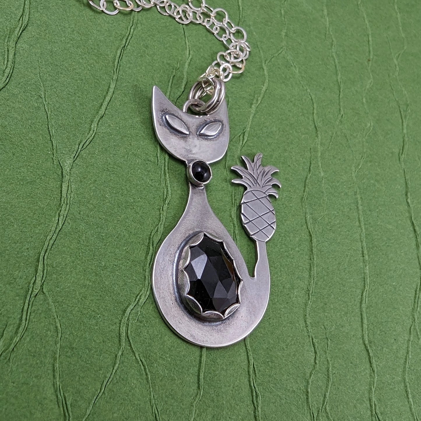 Sterling silver handmade cat with pineapple tail and rosecut onyx on a green background