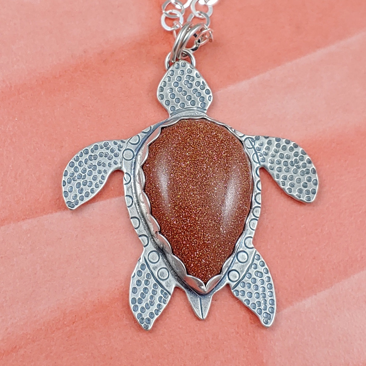 Sterling silver handmade sea turtle necklace with goldstone on orange background