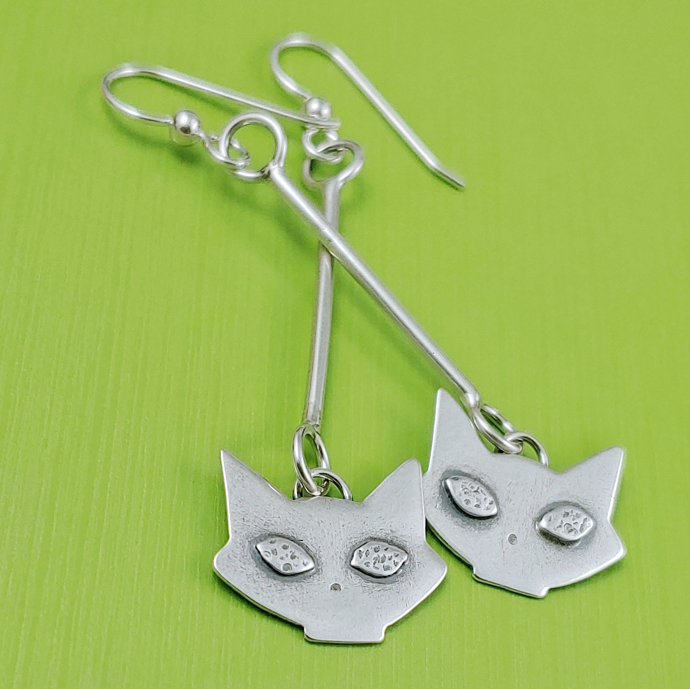Mid mod sterling silver cat head dangle earrings on a green background.