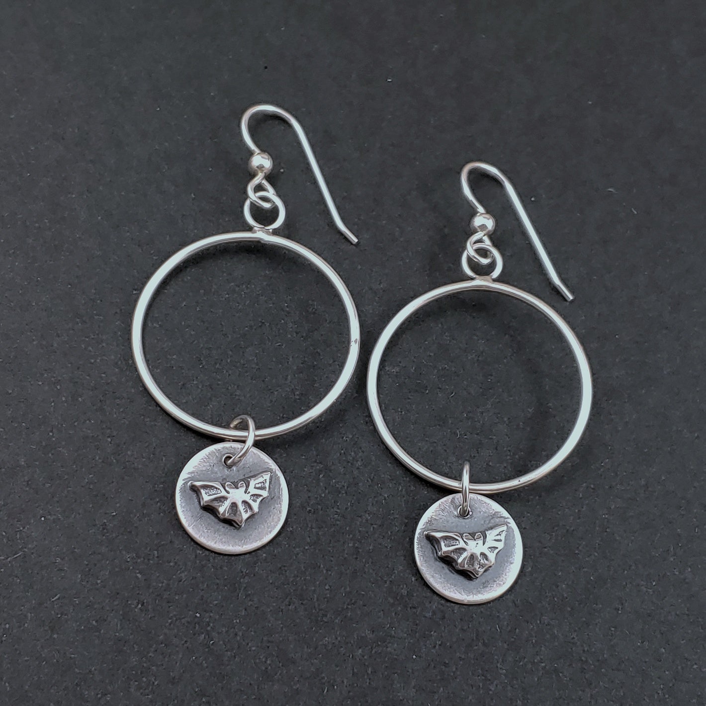 Photo of sterling silver hoops with small bat dangles.