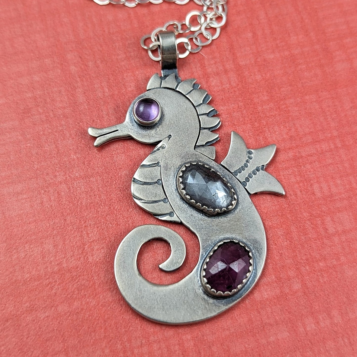 Sterling silver handmade seahorse with rosecut danburite and ruby with pink cubic zirconia eye on orange background