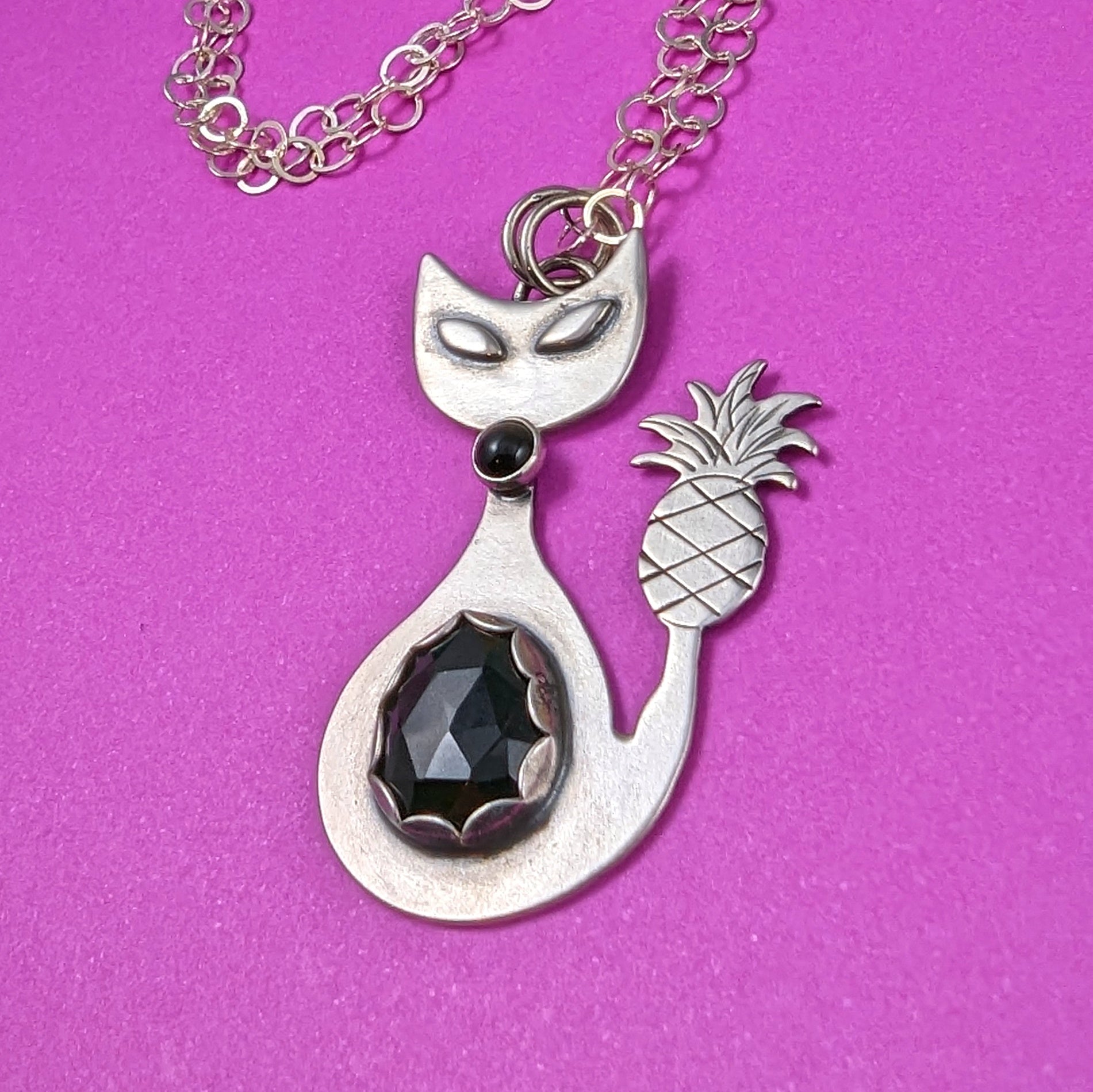 Sterling silver handmade cat with pineapple tail and rosecut onyx on a pink background