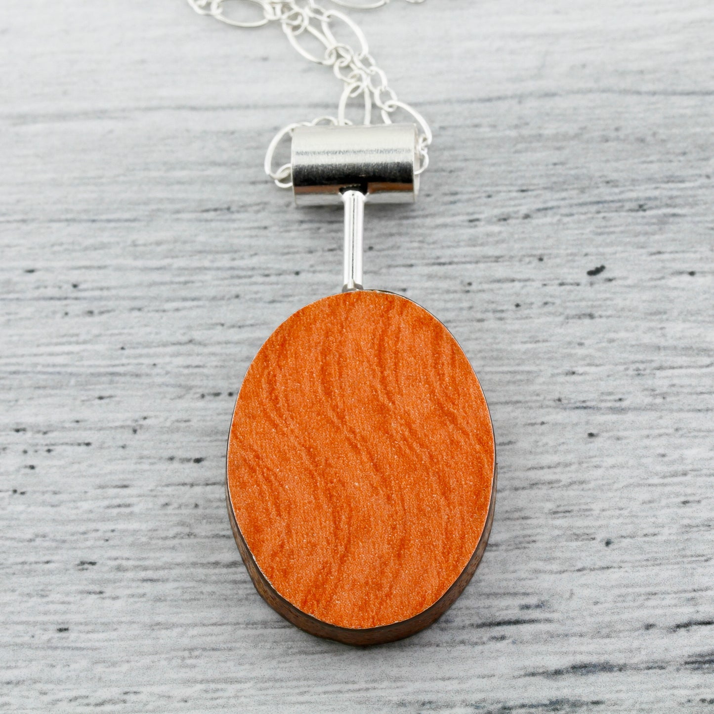Orange side of oval shaped contemporary art jewelry with laminate on wood