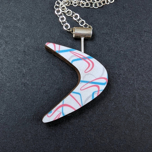 Boomerang shaped laminate on wood necklace on black background