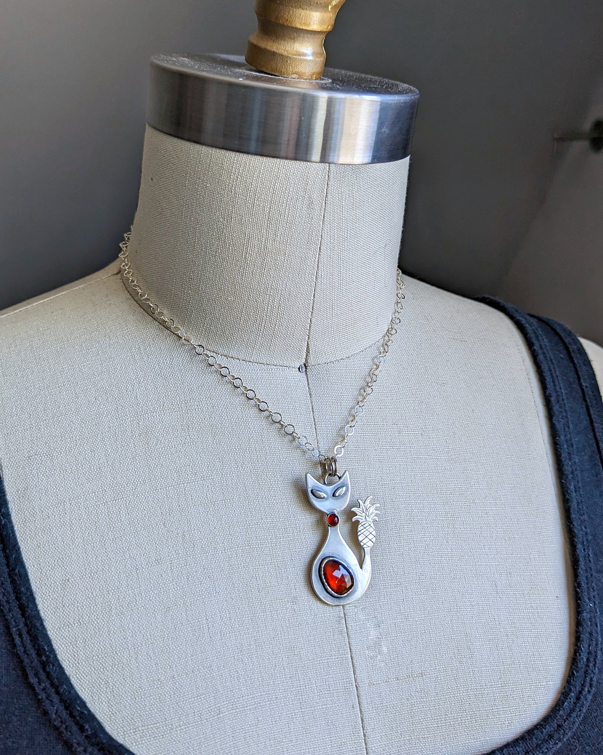 Sterling silver handmade cat with pineapple tail and garnet on a dress form