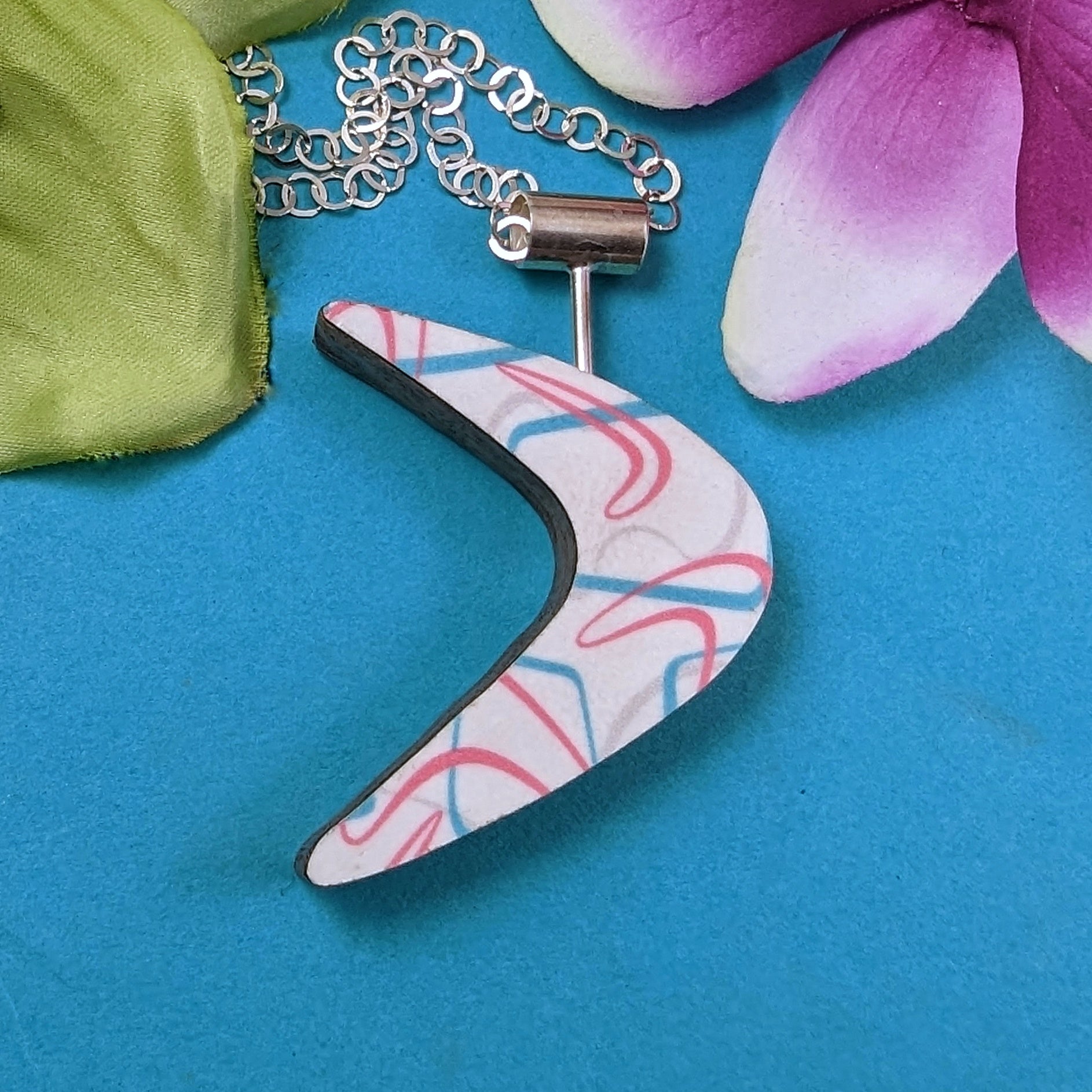 Boomerang shaped laminate on wood necklace on turquoise background