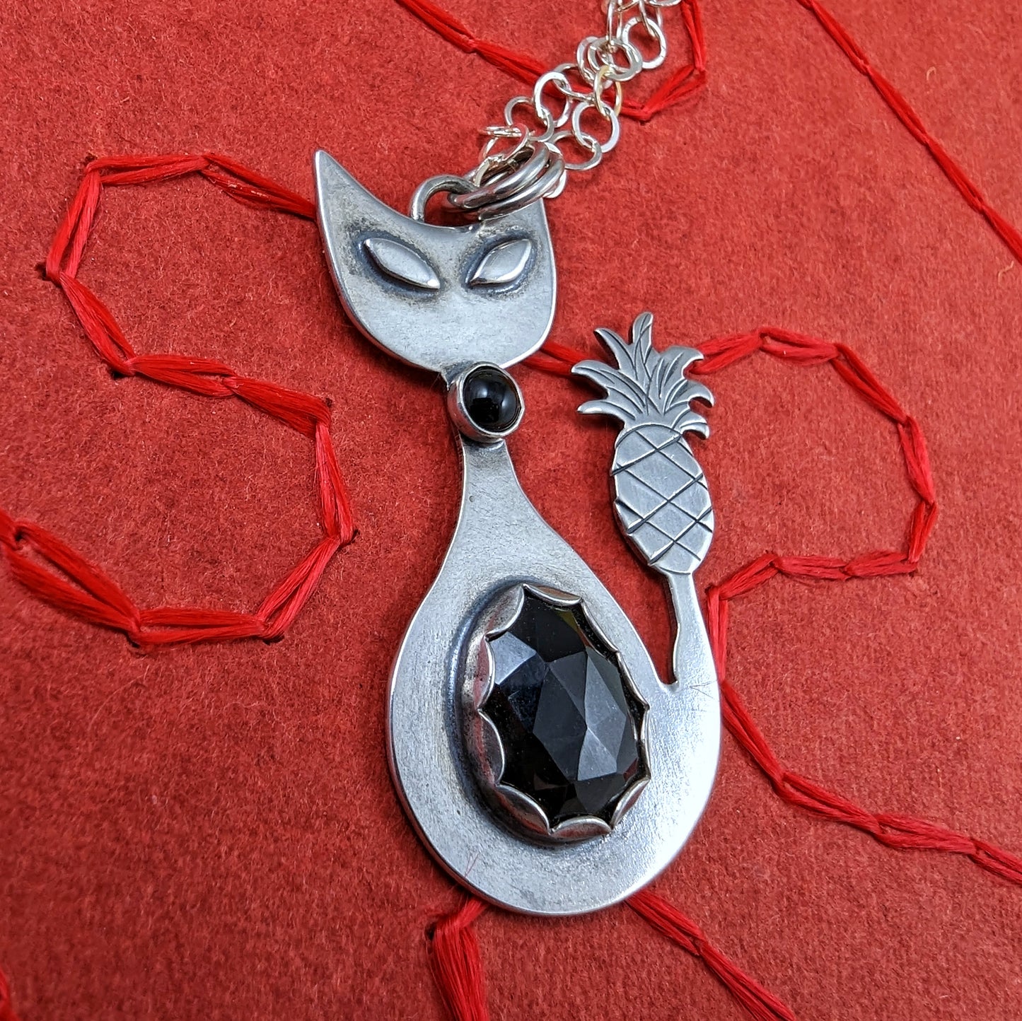 Sterling silver handmade cat with pineapple tail and rosecut onyx on a red background