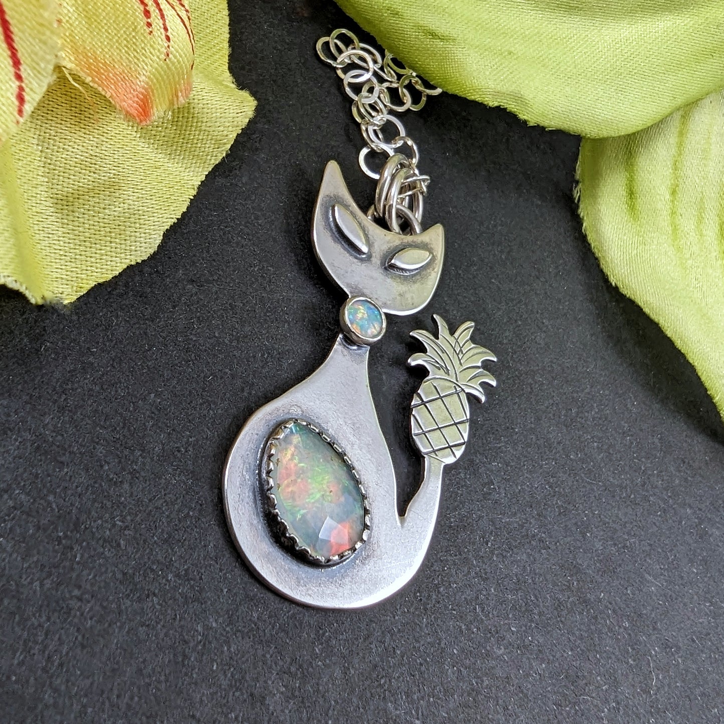 Sterling silver handmade cat with pineapple tail and Ethiopian opal on a black background and flowers